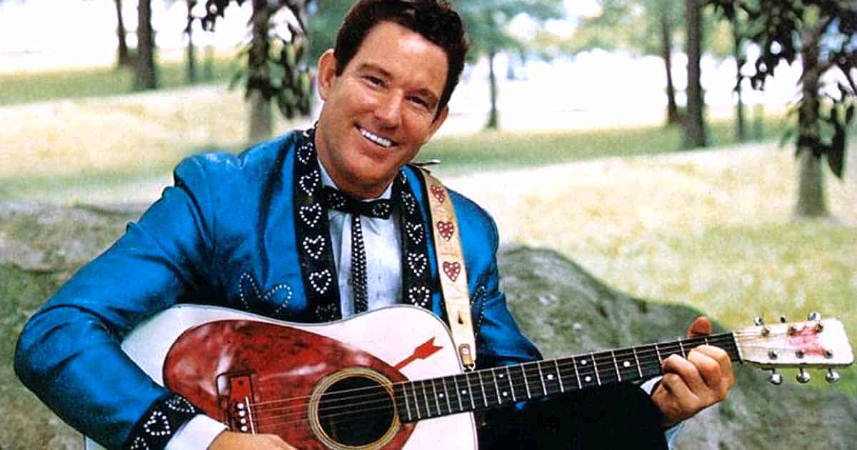 Freddie Hart poses with his guitar and a big smile before the camera.