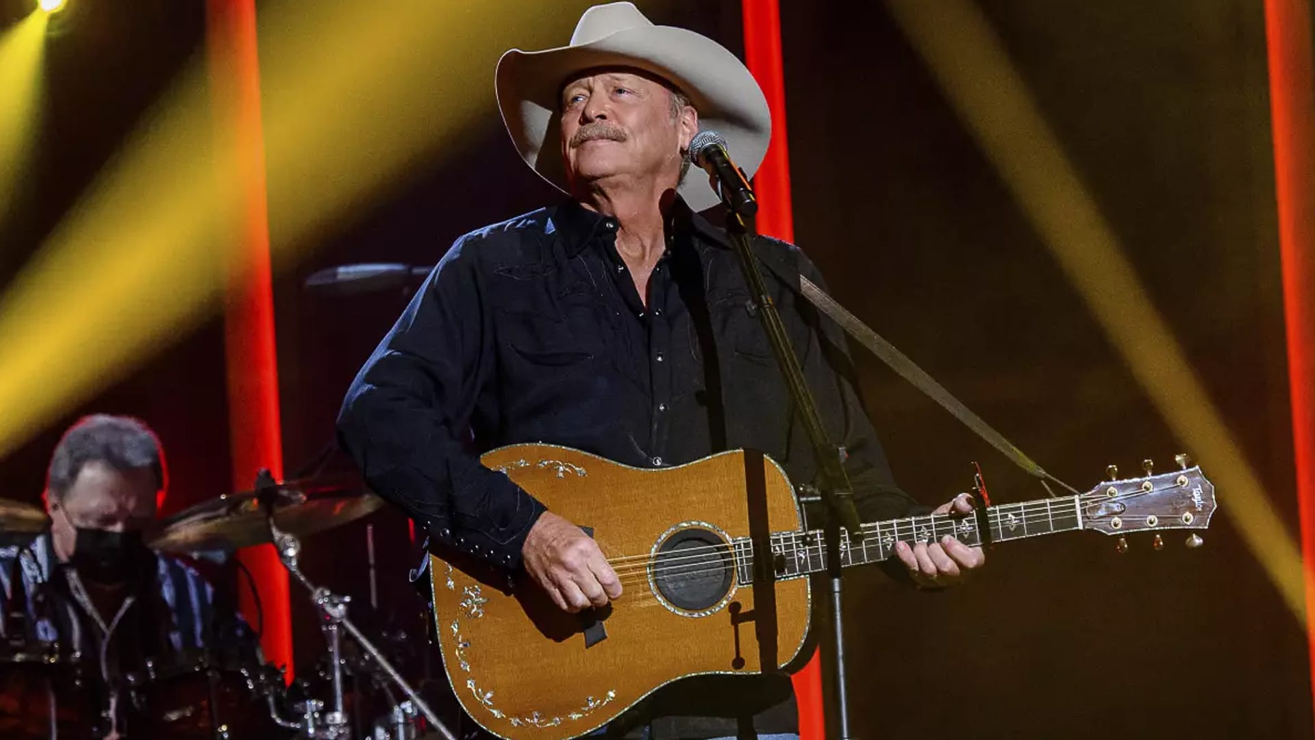 Alan Jackson performs onstage under warm lights during his Last Call Tour, wearing his signature cowboy hat and strumming a guitar.