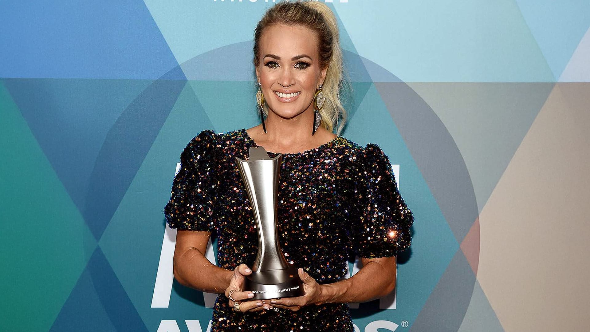 Carrie Underwood smiles while holding her ACM Award, celebrating her record as the woman with the most Entertainer of the Year wins.
