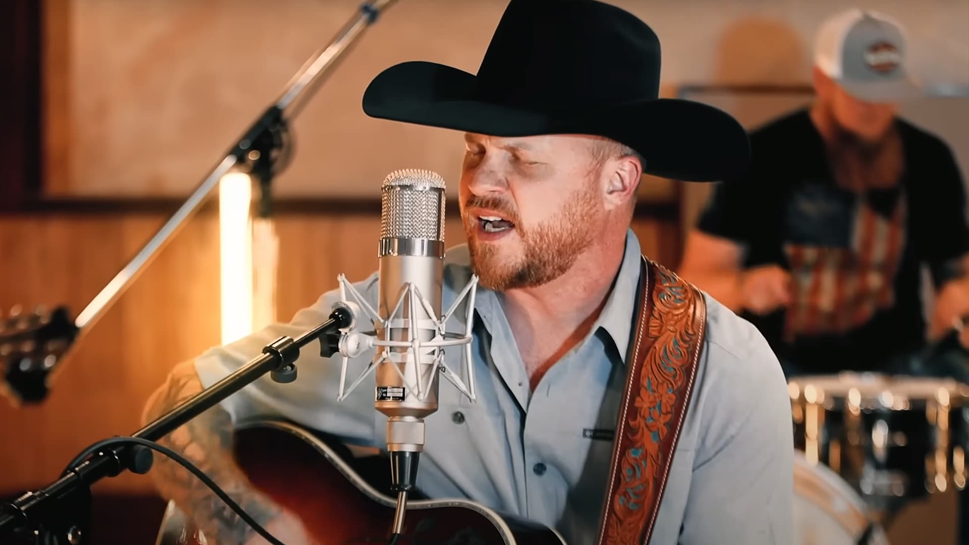 Cody Johnson performing an acoustic set, sitting with a guitar in hand and eyes closed, delivering a raw and emotional version of “Travelin’ Soldier”.