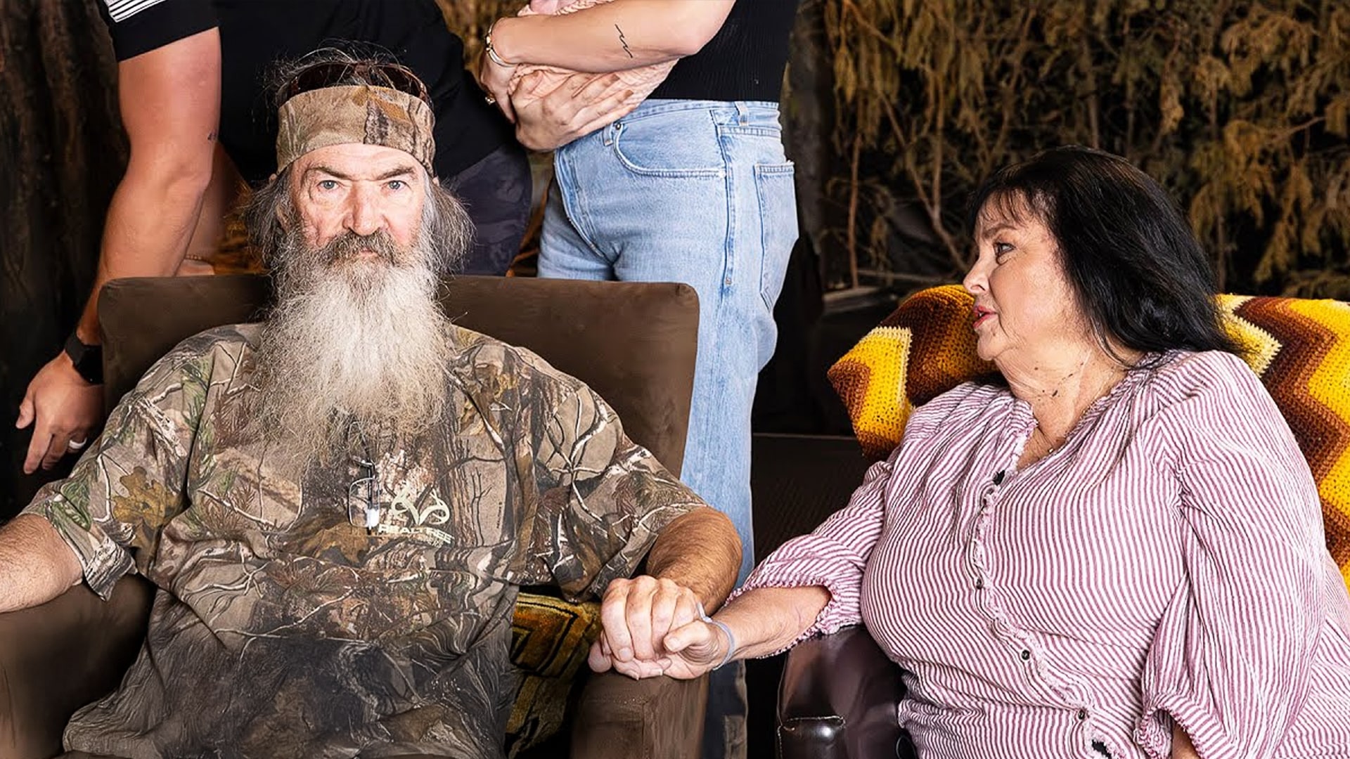 Phil Robertson and Miss Kay Robertson from Duck Dynasty hold hands and sit side-by-side in a care facility, reunited after months apart due to health concerns.
