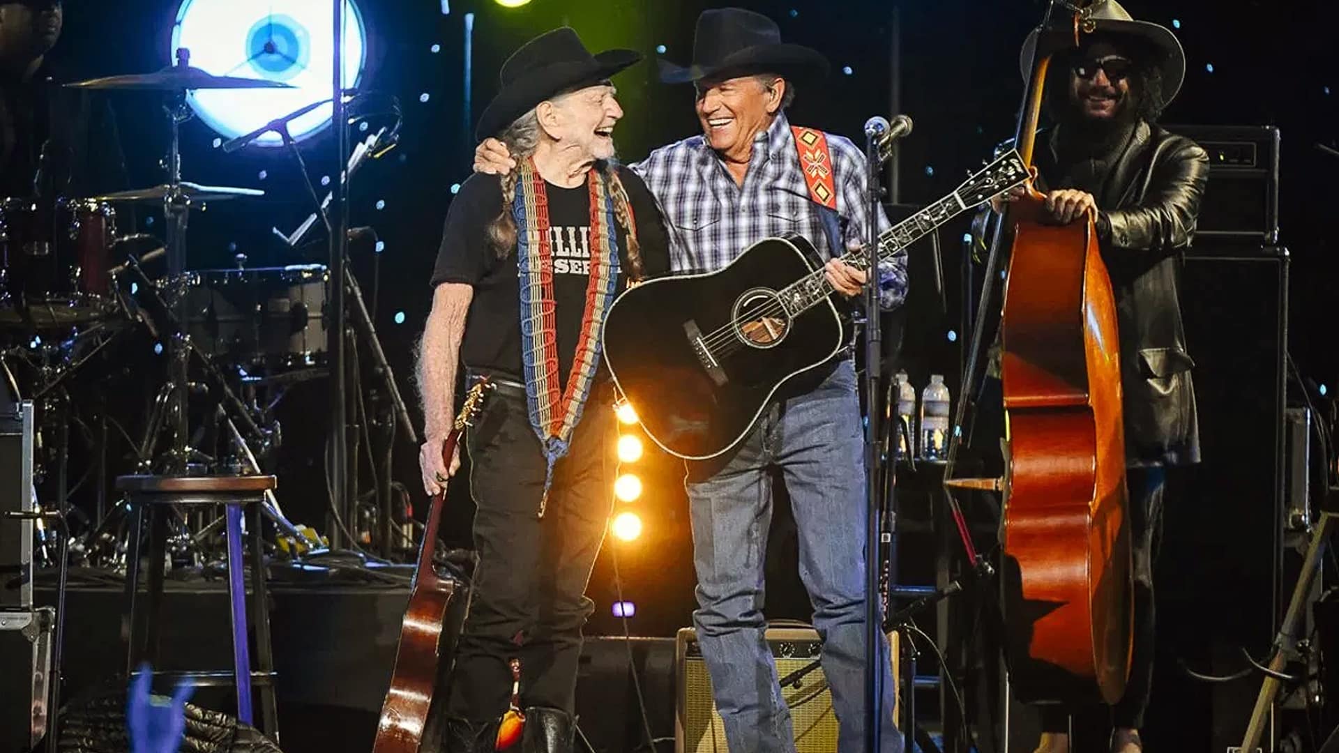 Willie Nelson and George Strait smile and share a warm moment onstage, each holding a guitar, during their first-ever duet performance at a tribute concert.
