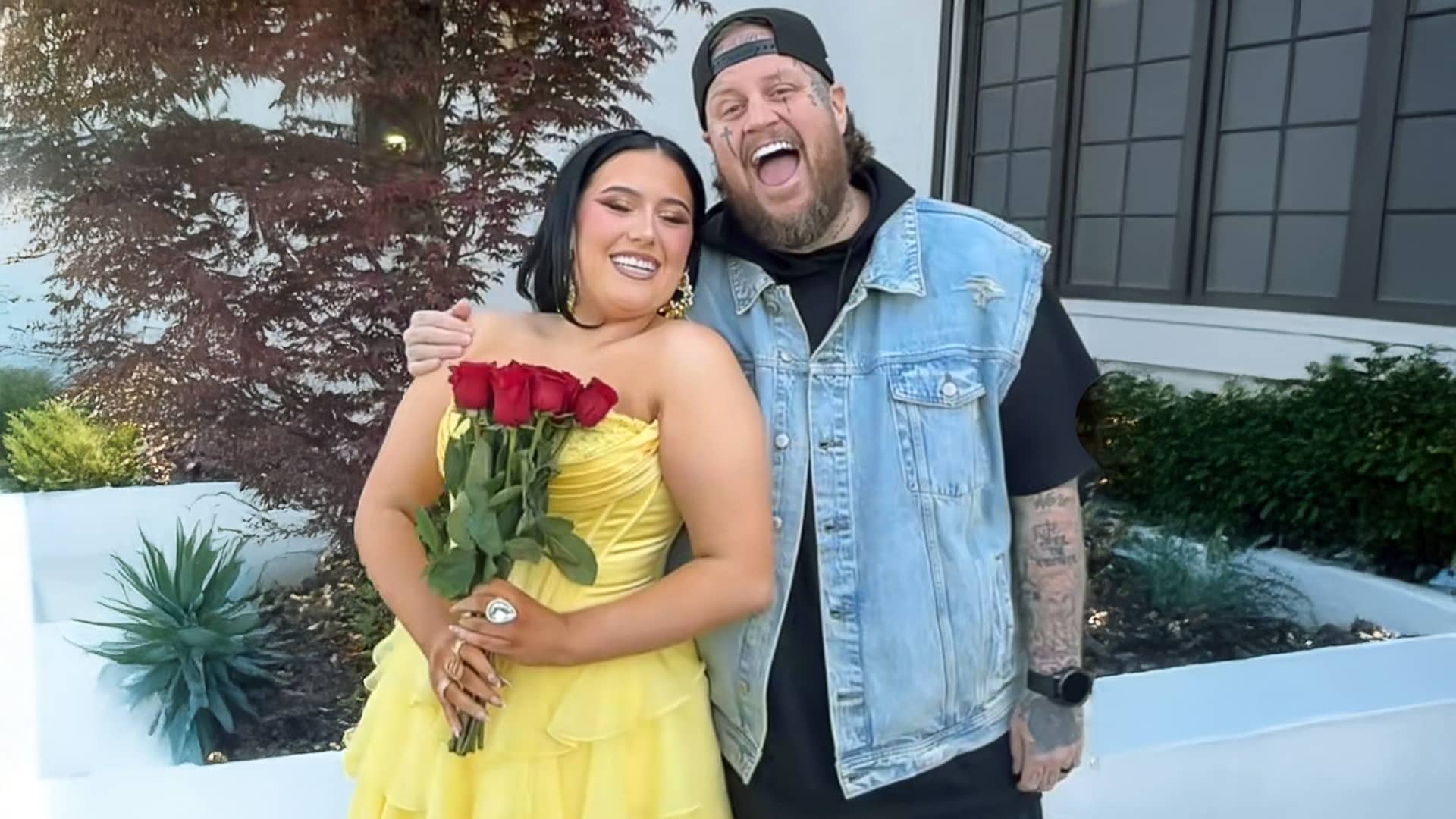 Jelly Roll beams with pride as he hugs his daughter Bailee, dressed in a yellow prom gown and holding red roses, capturing a heartfelt father-daughter moment.