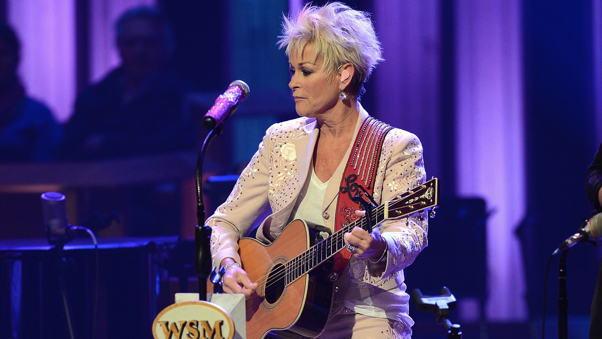 Lorrie Morgan performs at the Grand Ole Opry with a somber expression, now pausing her tour as her husband Randy White battles a serious health crisis.