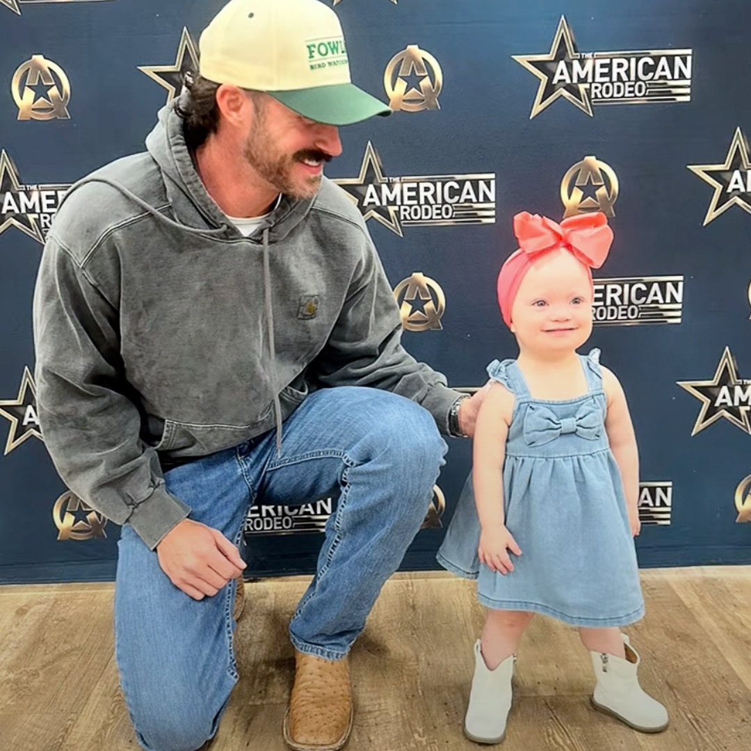 Riley Green smiles as he shares a sweet moment with toddler fan Hadley, who stands in boots and a big pink bow at The American Rodeo meet-and-greet.
