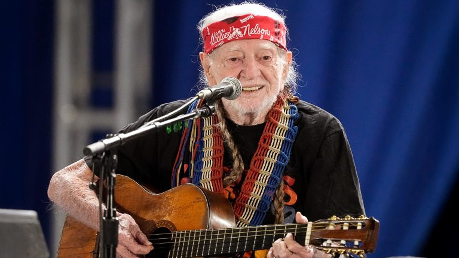 Willie Nelson beams while playing guitar on stage at 91 years old, embodying the joyful energy and simple, healthy habits that keep him thriving and touring into his ninth decade.