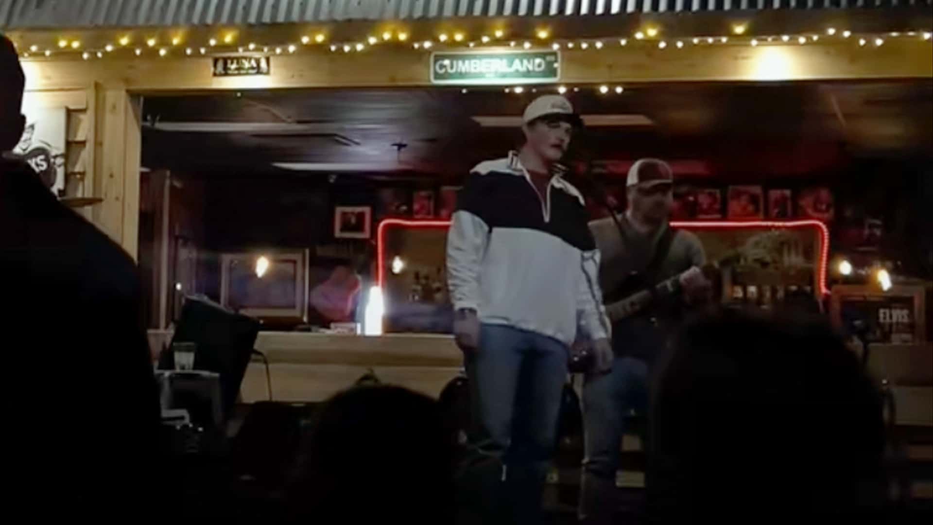 Zach Top stands onstage at a dimly lit Nashville dive bar, mid-performance, singing Merle Haggard's "Ramblin' Fever" with a guitarist behind him.