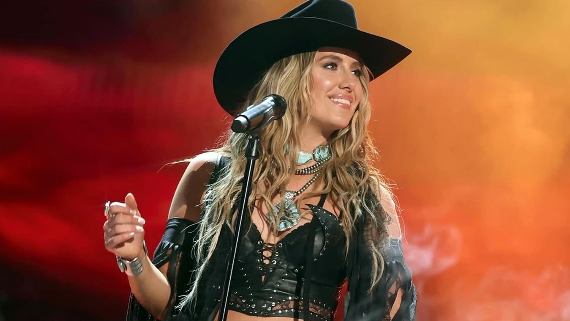 Lainey Wilson performs onstage in black fringe and turquoise jewelry, radiating confidence built from years of grit, hustle, and hard-earned success.