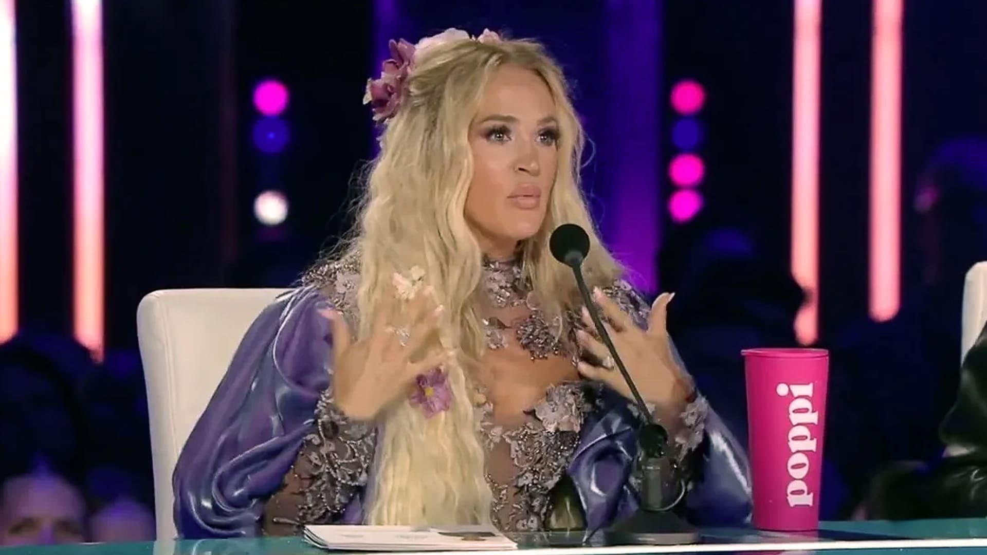 Carrie Underwood speaks passionately as a guest judge on American Idol, wearing a floral purple outfit, while fans react online to her controversial critique.