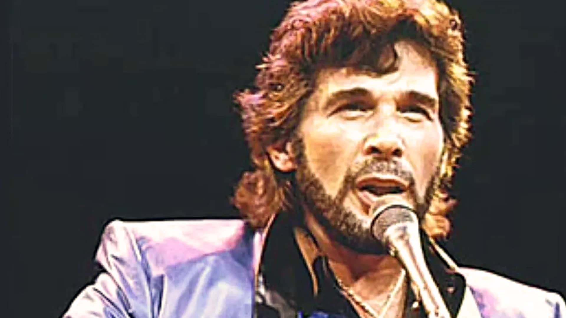 Eddie Rabbitt performs passionately on stage in a colorful jacket, representing a forgotten era when his smooth voice and songwriting shaped the future of country music.