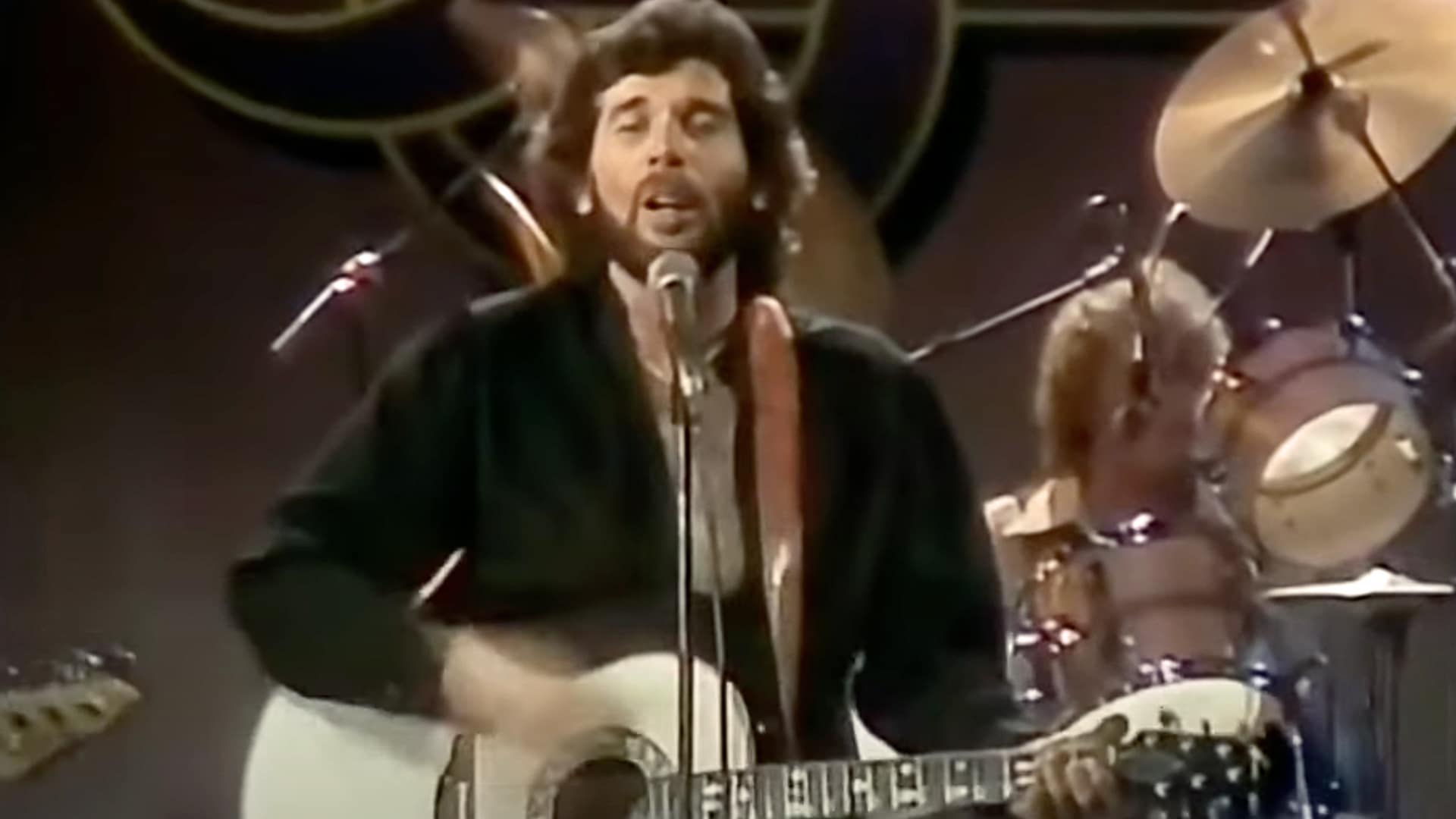 Eddie Rabbitt performs "Drivin' My Life Away" with his guitar on stage, delivering one of country music's most iconic road anthems with timeless energy and grit.