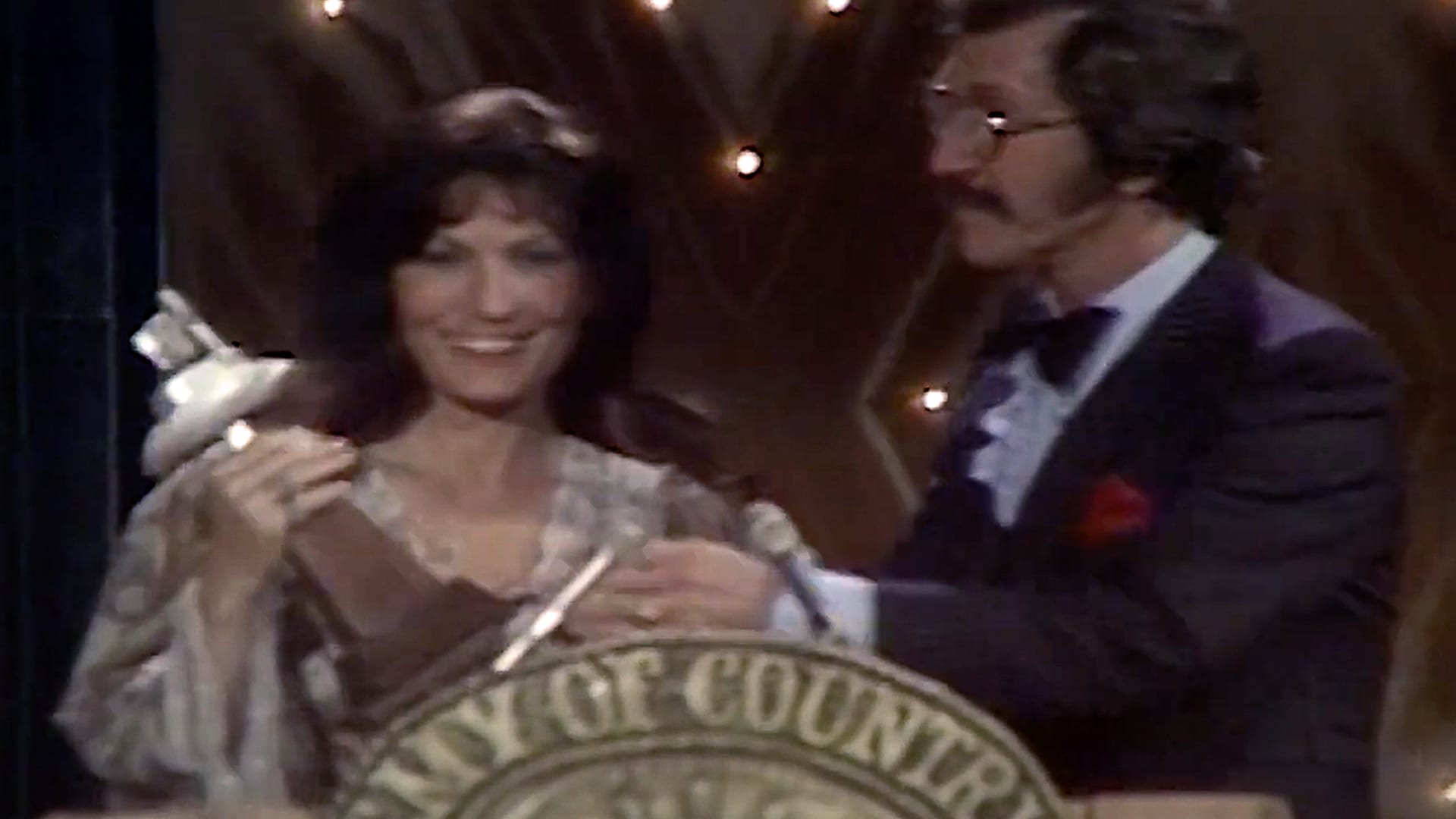 Loretta Lynn smiles while holding her Entertainer of the Year trophy at the 1976 ACM Awards, becoming the first woman to receive the honor in country music history.