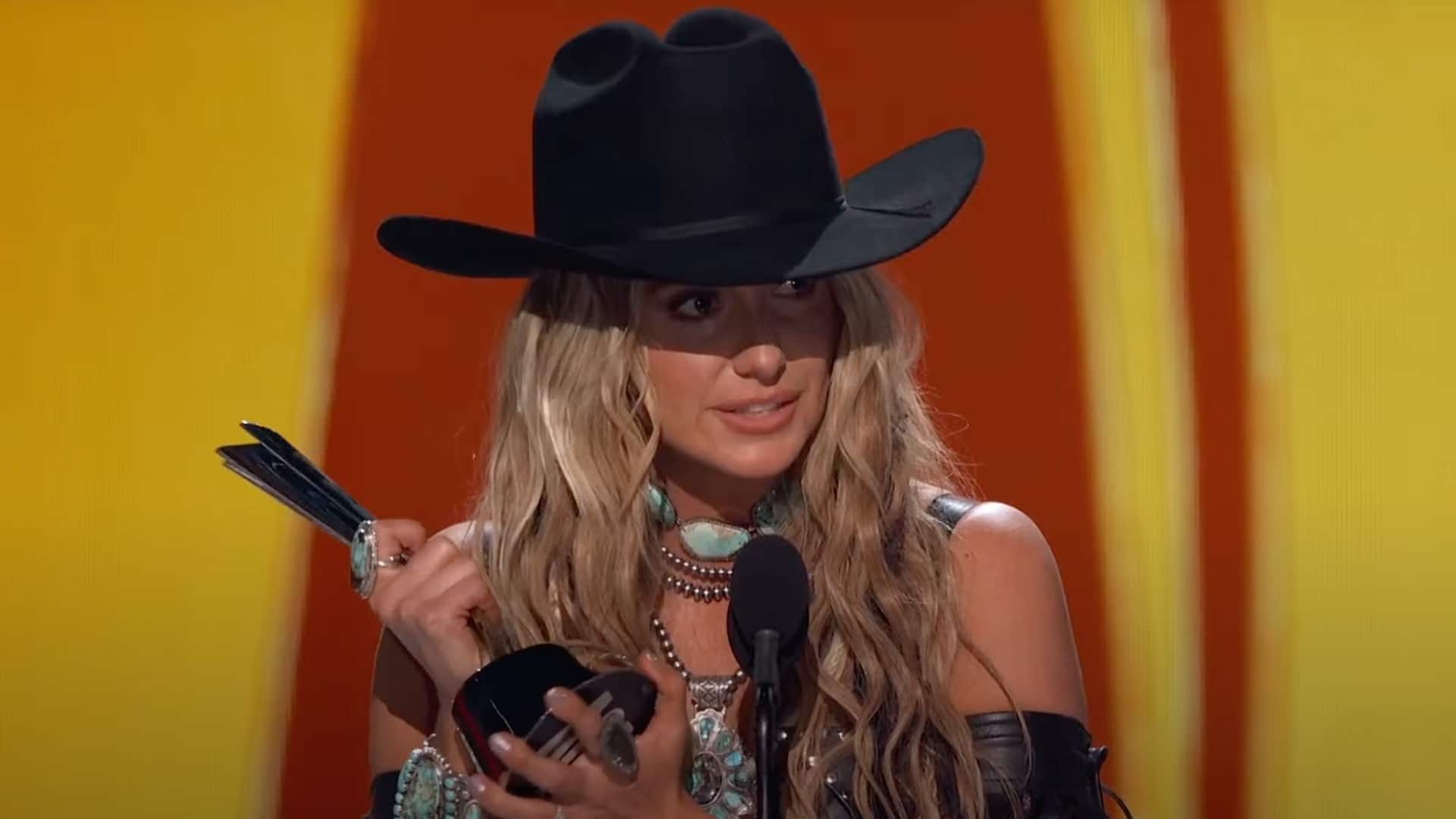 Lainey Wilson holds her ACM trophy with emotion while delivering her acceptance speech for Album of the Year at the 2025 ACM Awards, dressed in her signature black cowboy hat and turquoise jewelry.