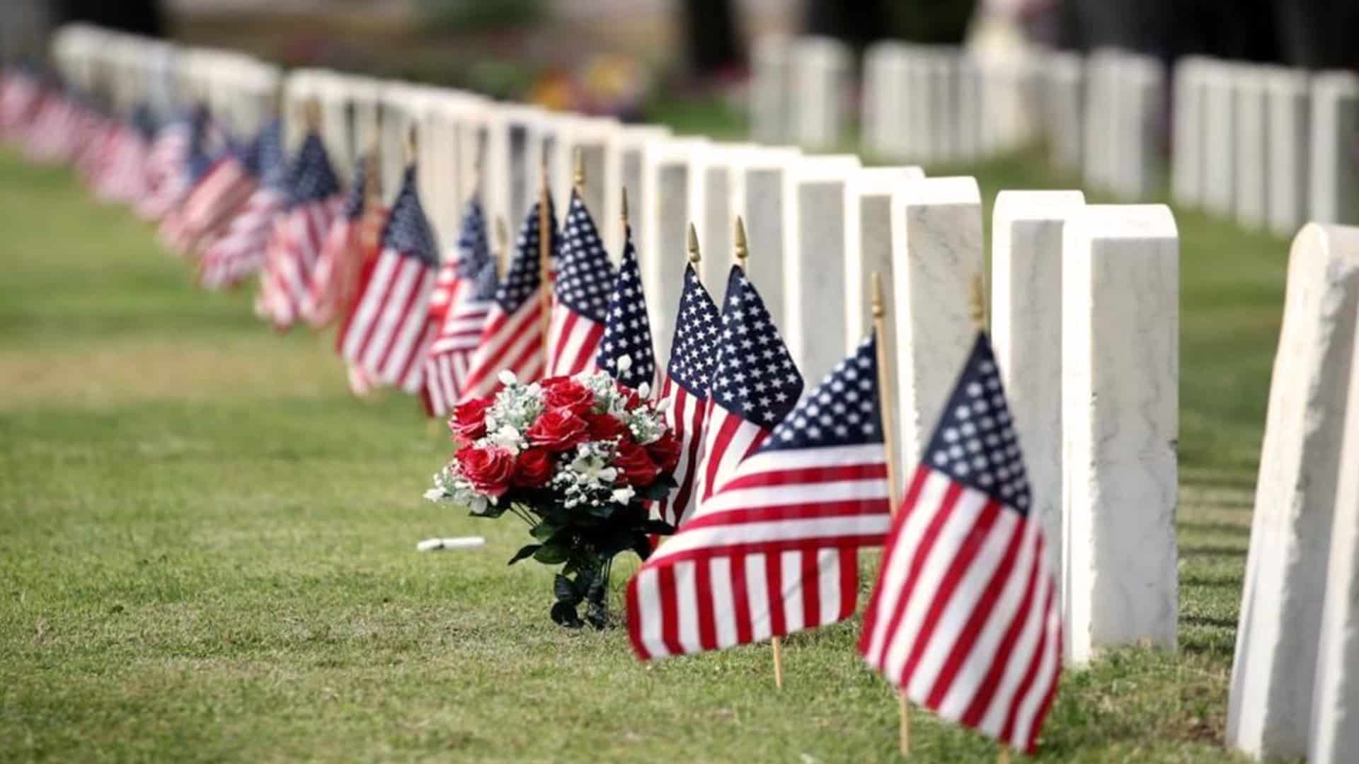 American flags and flowers placed by headstones in a military cemetery, symbolizing the true purpose of Memorial Day—honoring the fallen, not to be confused with Veterans Day.