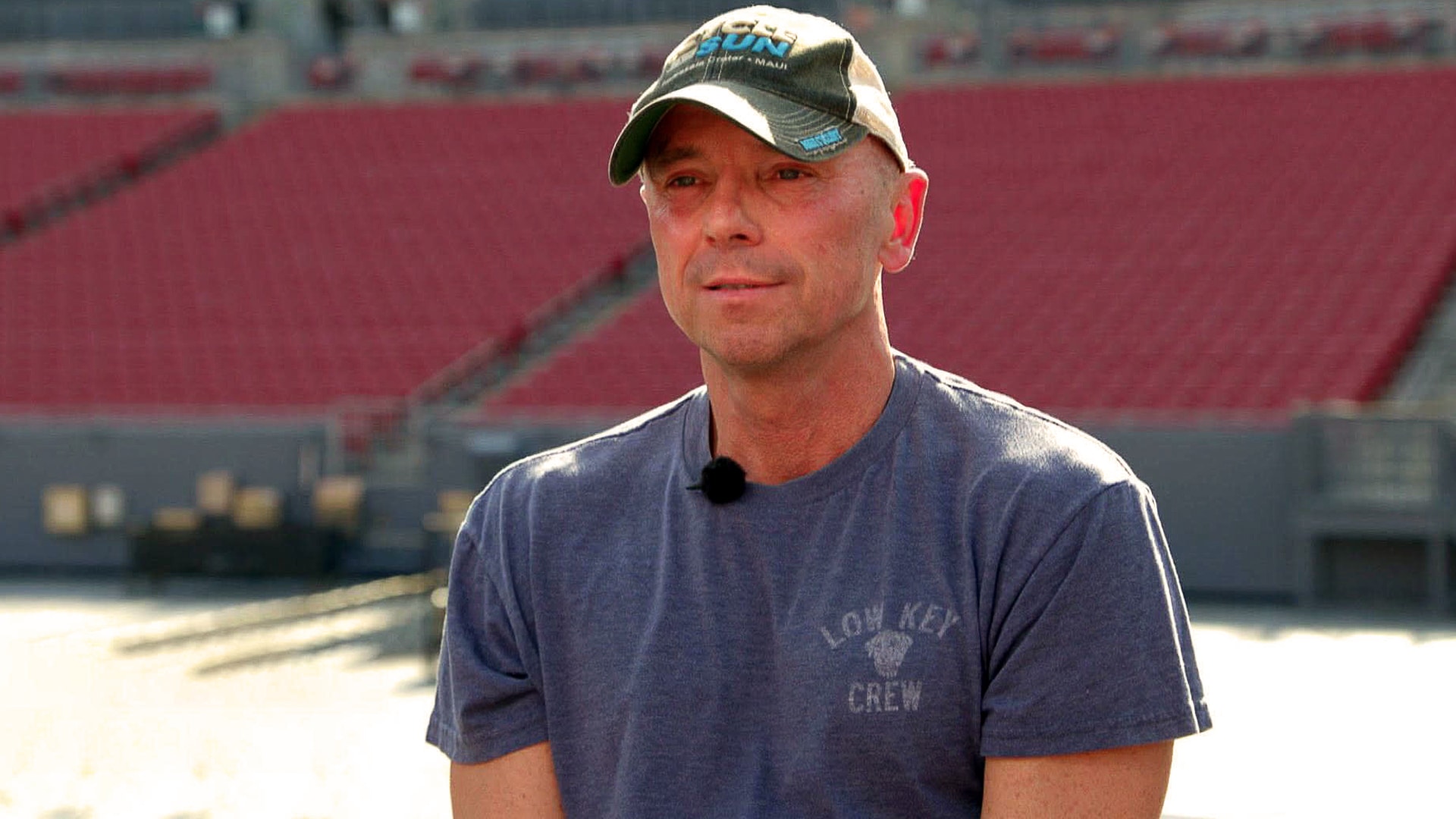 Kenny Chesney sits casually in an empty stadium, wearing a ballcap and “Low Key Crew” T-shirt, addressing long-standing rumors with calm clarity.