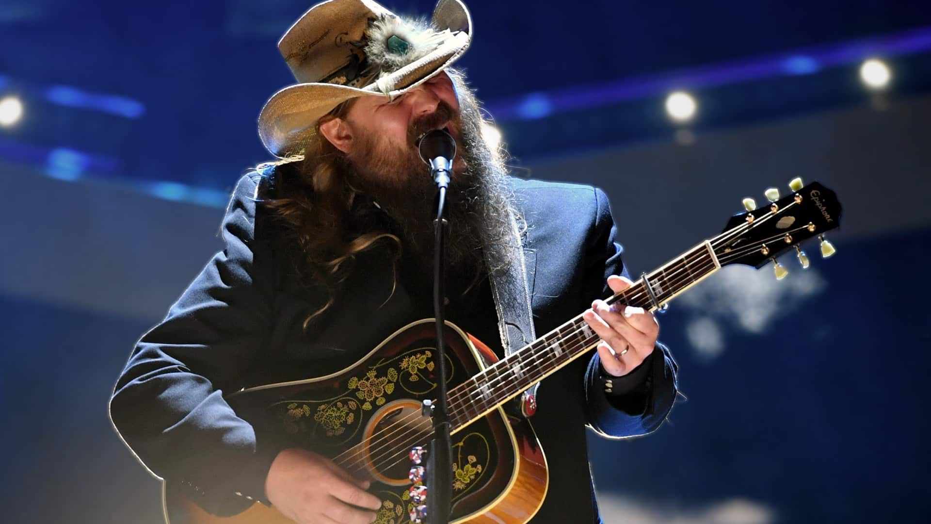 Chris Stapleton performs onstage in a cowboy hat and embroidered guitar, passionately singing under dramatic lighting before a show that never made it to Greenville.