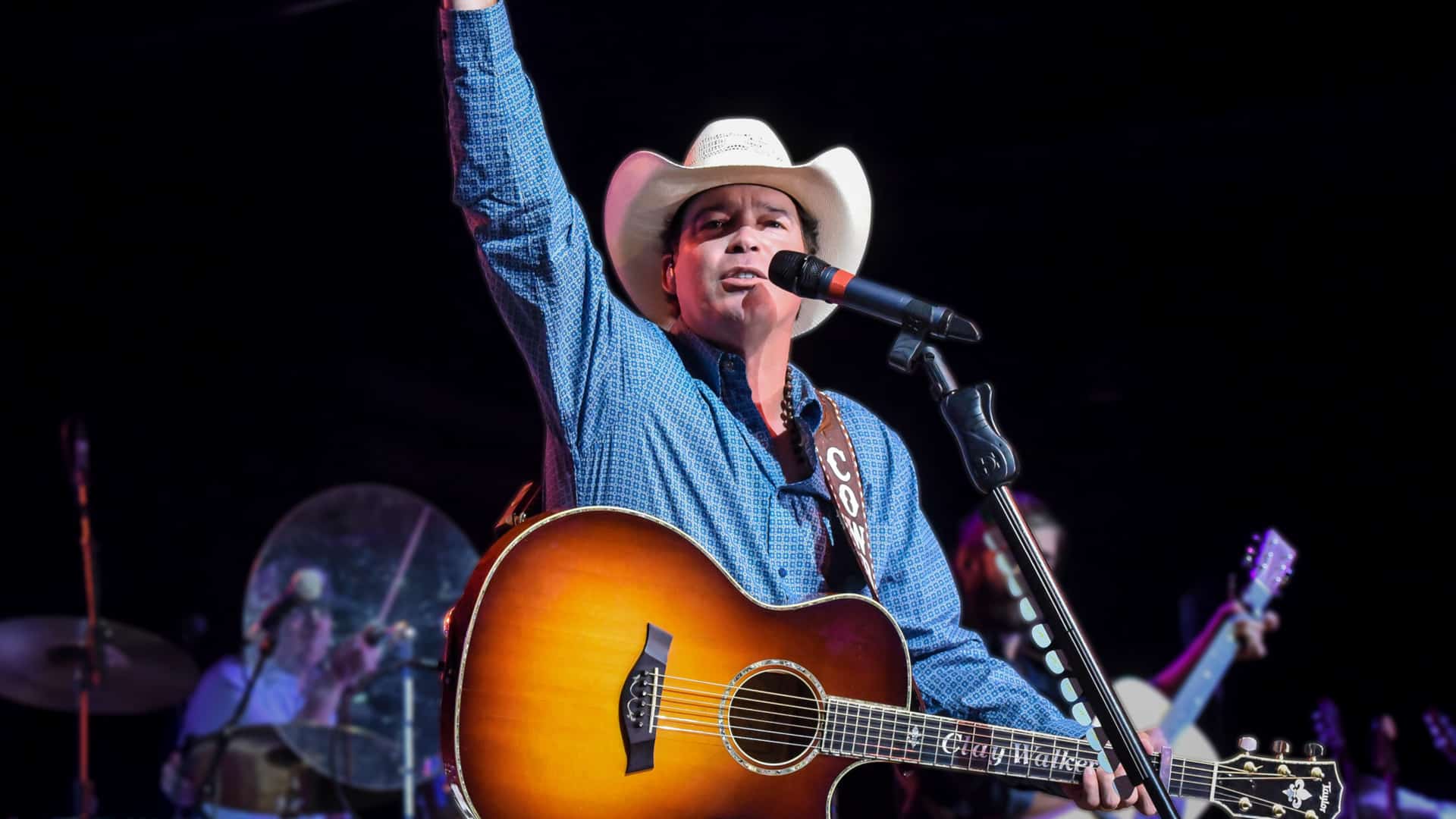 Clay Walker raises his arm mid-performance, guitar in hand, as he prepares to headline Nashville's Ryman Auditorium.