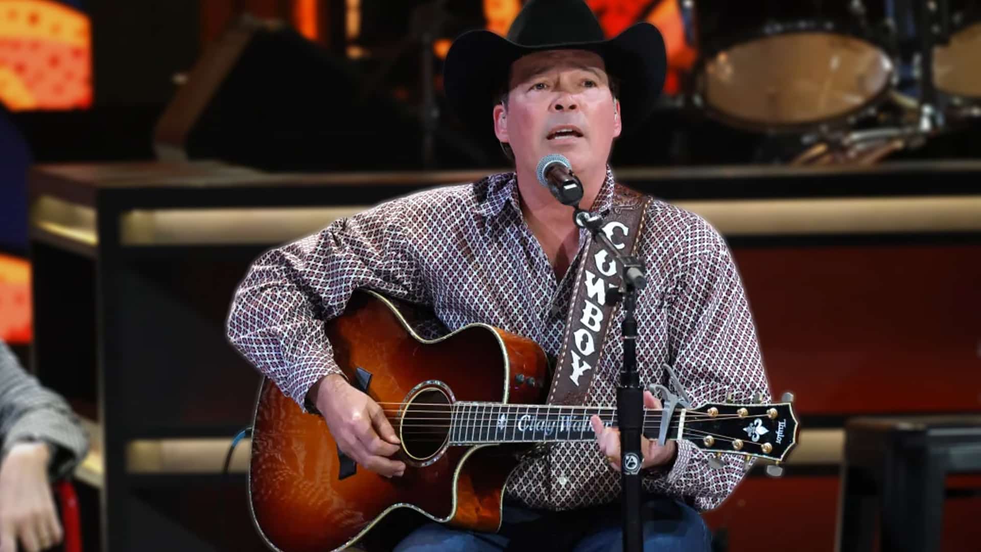 Clay Walker plays guitar onstage with focus and grit, wearing a cowboy hat and “COWBOY” strap as he battles MS at 55.