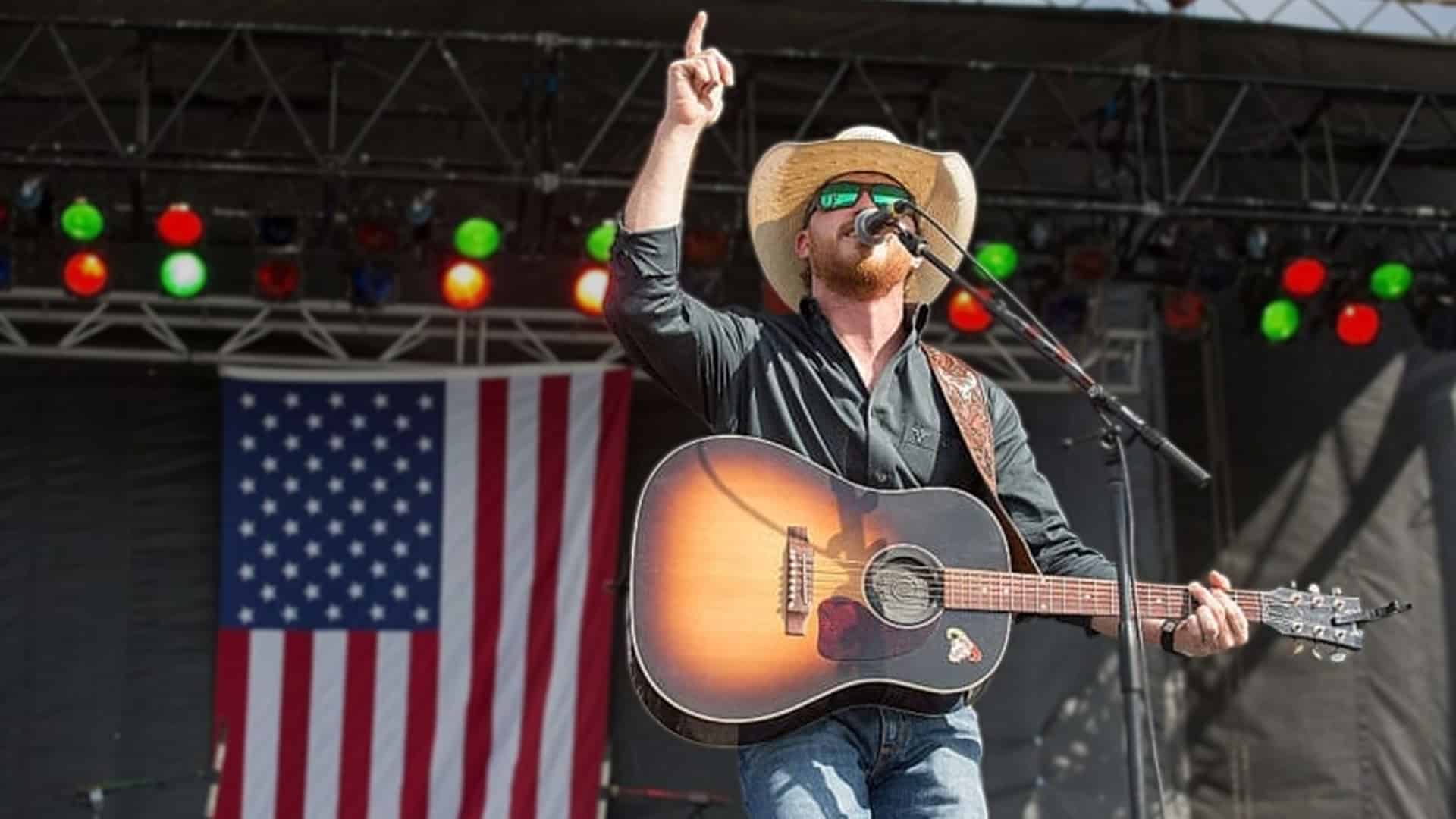 Cody Johnson performs at an outdoor concert in front of an American flag, shown here during a previous show, before he paused his Tailgate N Tallboys set to address anti-Trump protests and lead the crowd in a "God Bless America" sing-along.