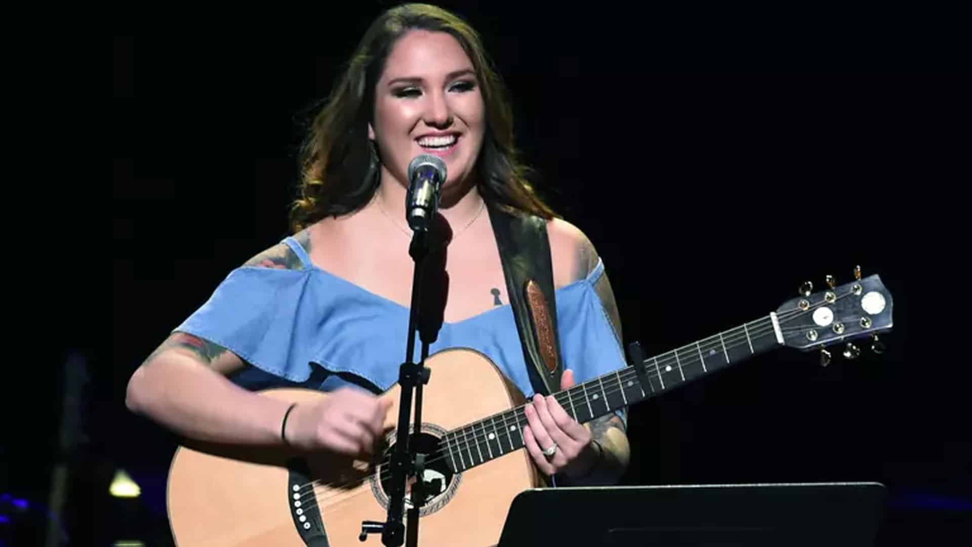 Allie Colleen performs on stage with a big smile and acoustic guitar, showing confidence and independence as she builds her music career on her own terms—far from her father Garth Brooks’ shadow.