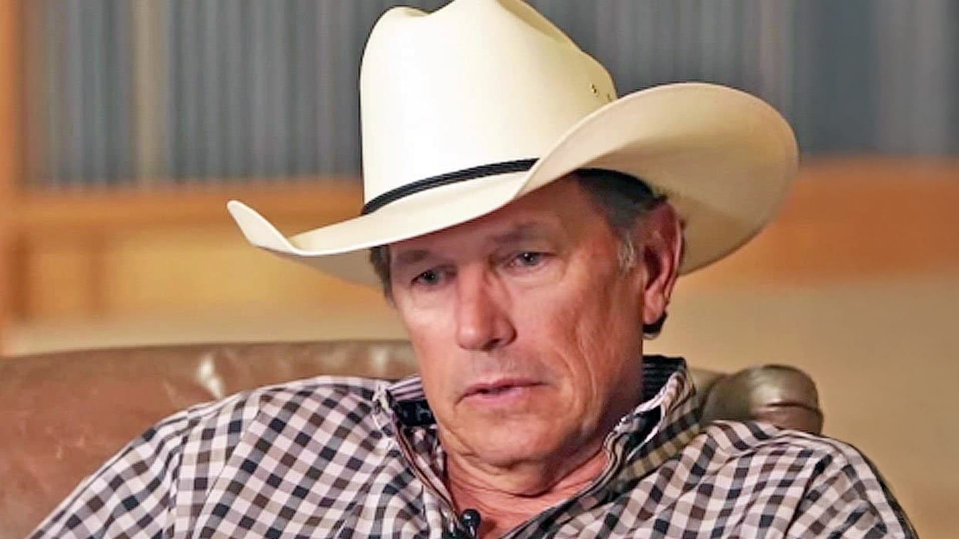 George Strait sits somber in a cowboy hat and checkered shirt, reflecting the quiet grief behind his song "You'll Be There."