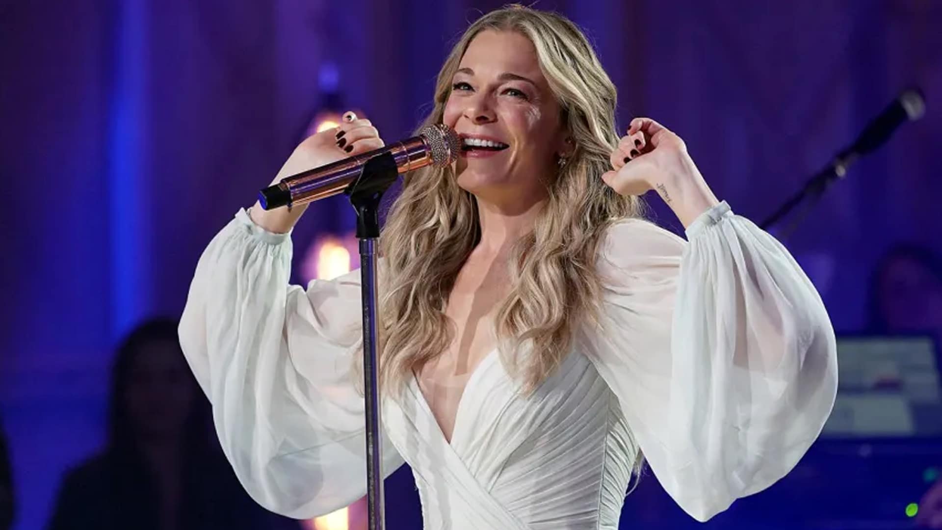 LeAnn Rimes smiles during a live performance in a flowing white dress, not from the moment of her dental mishap.