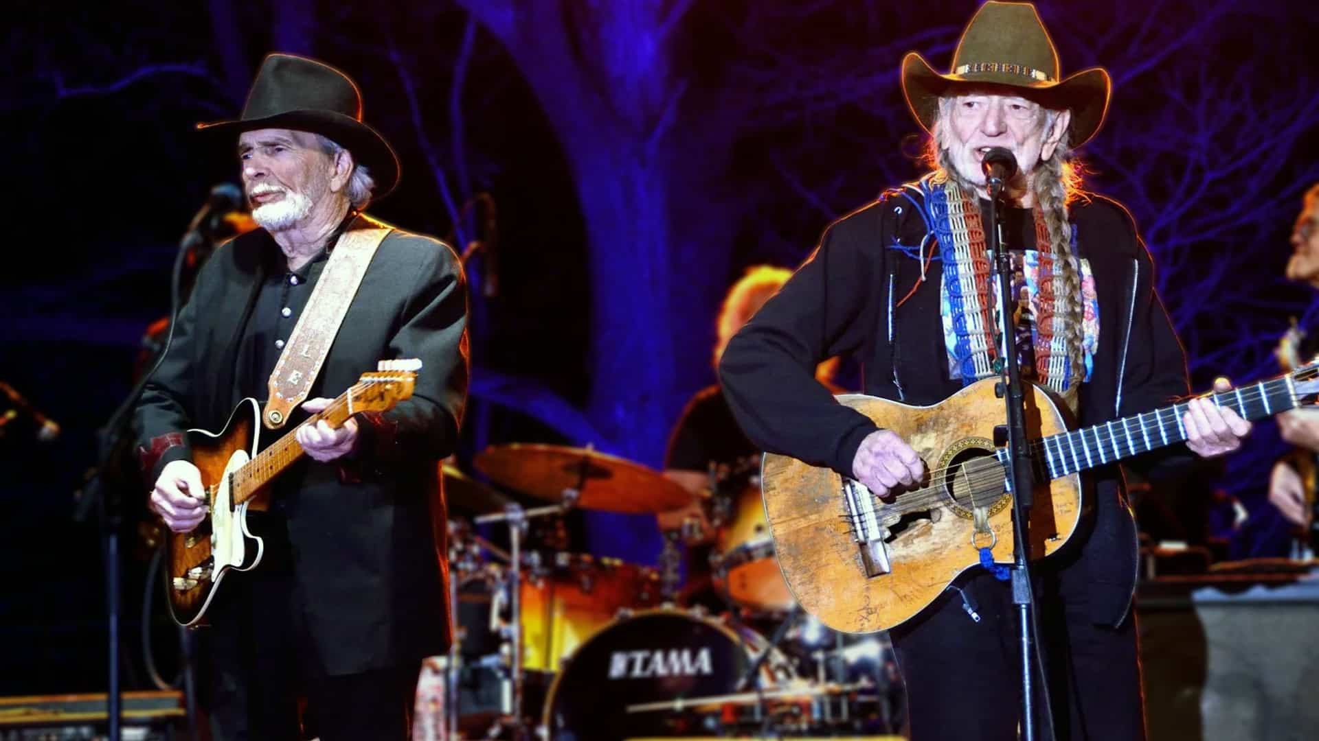 Willie Nelson and Merle Haggard perform on stage together in 2015, each playing a guitar and singing into microphones, proving their legendary status with the success of their album Django and Jimmie.