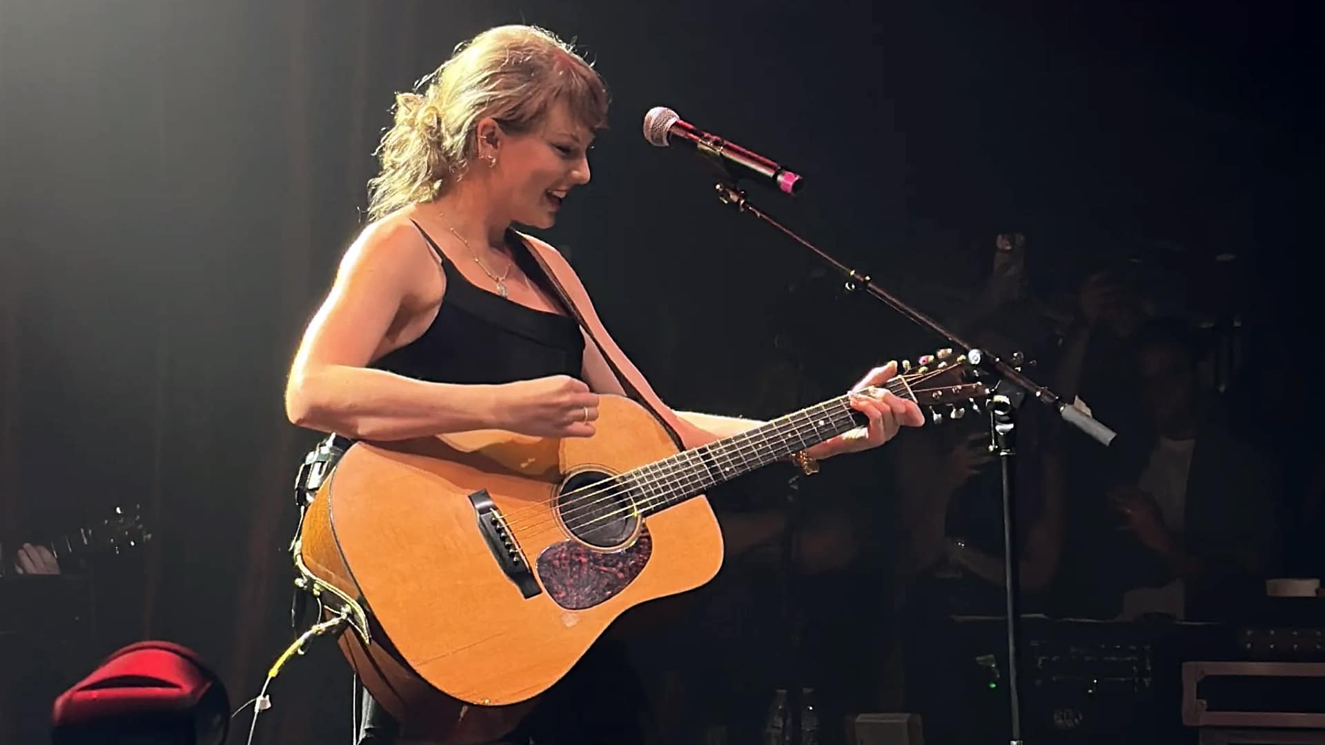 Taylor Swift smiles while strumming a guitar onstage in Nashville, sparking rumors about a possible country music return.