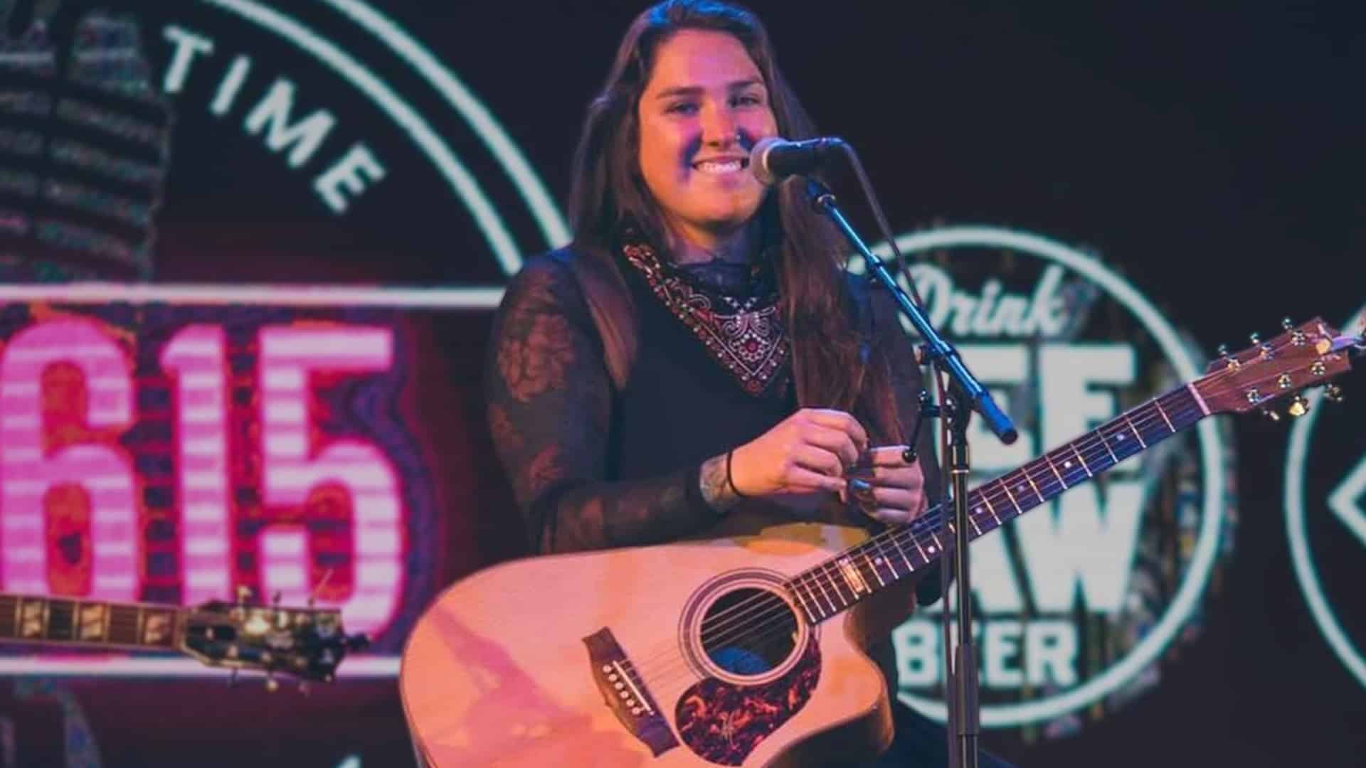 Allie Colleen stands onstage with a guitar, smiling confidently into the mic, determined to make her own musical legacy.