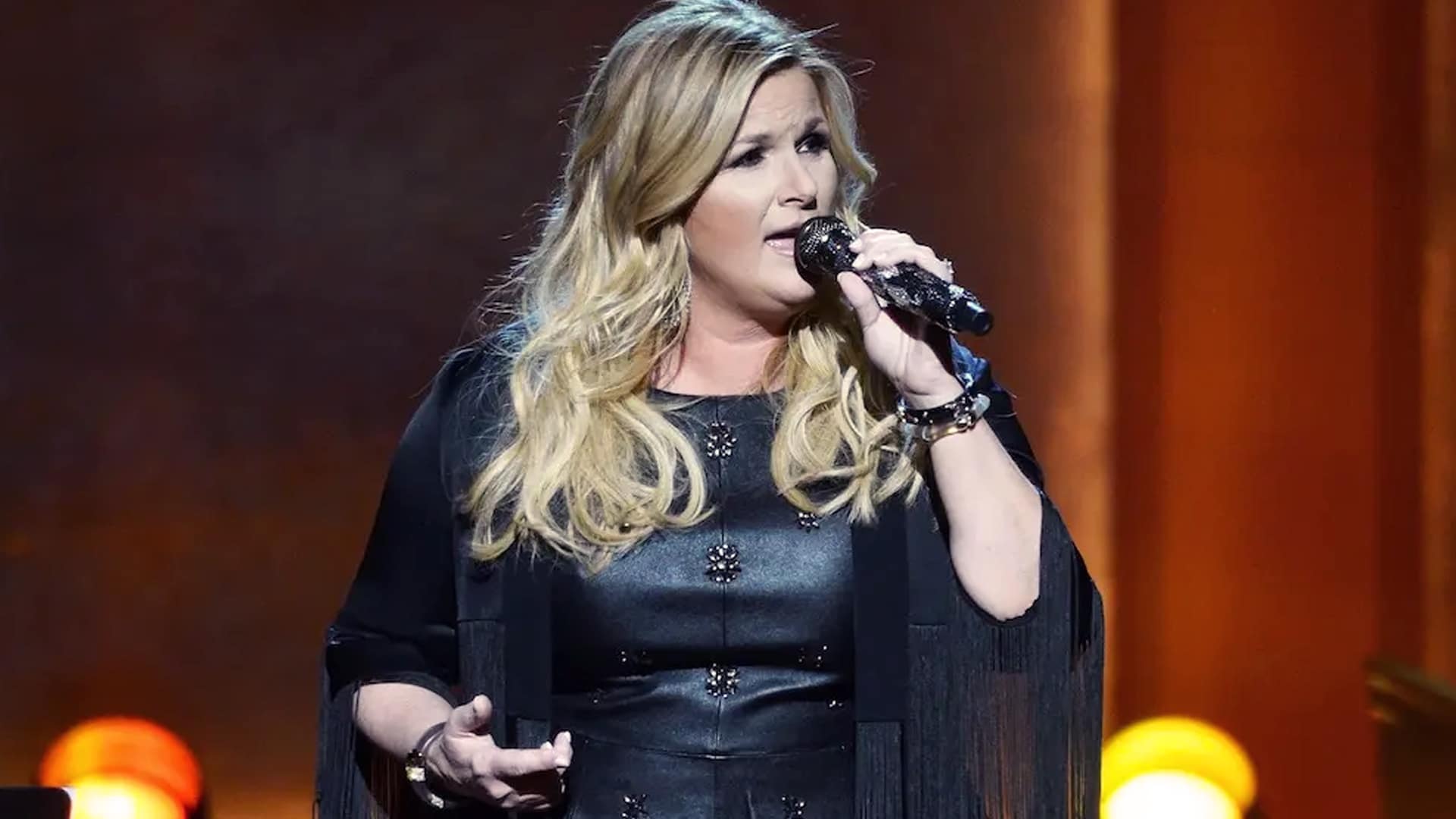 Trisha Yearwood performs passionately on stage in a black fringe dress, set to headline a benefit concert in Santa Barbara supporting first responders and wildfire-affected musicians.