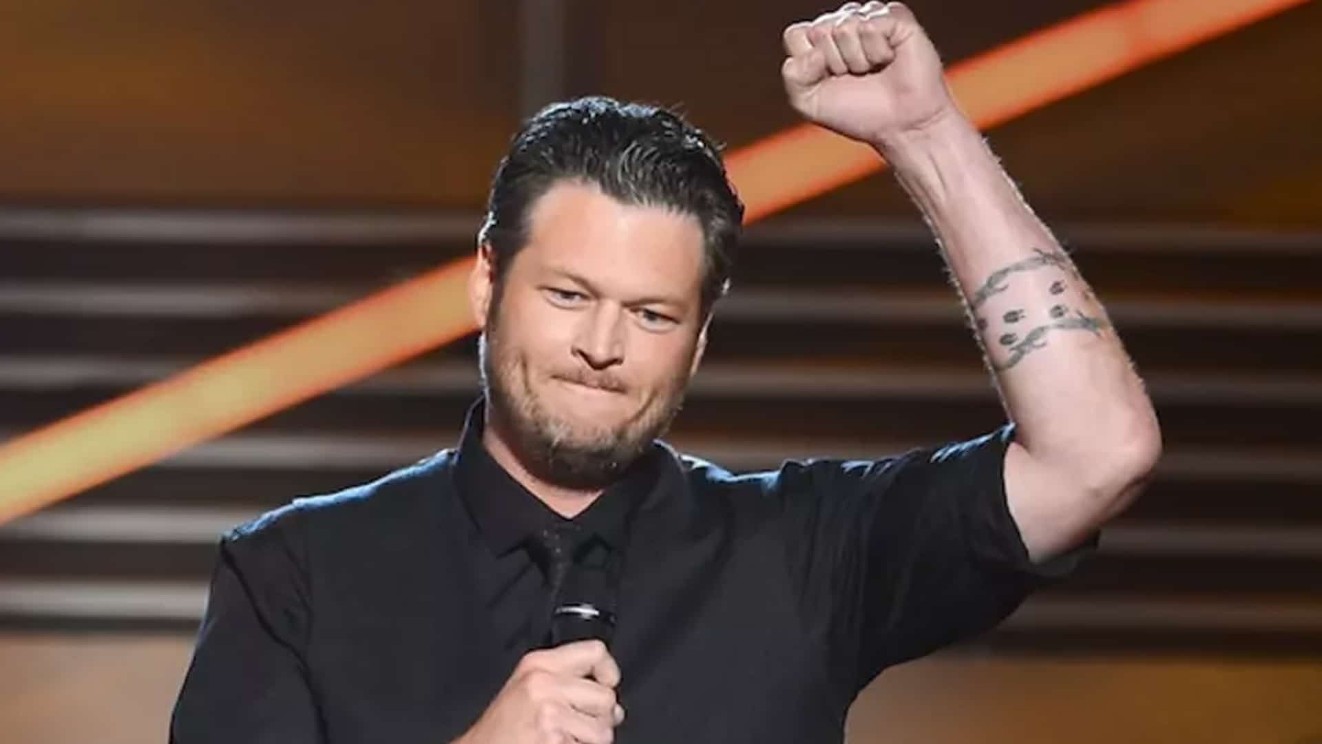Blake Shelton raises his fist while speaking into a microphone, reflecting on childhood struggles with music and pageants.