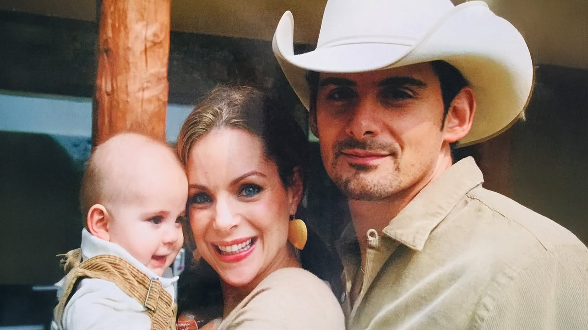 Brad Paisley in a cowboy hat smiles beside Kimberly Williams-Paisley and their baby in a warm family moment.