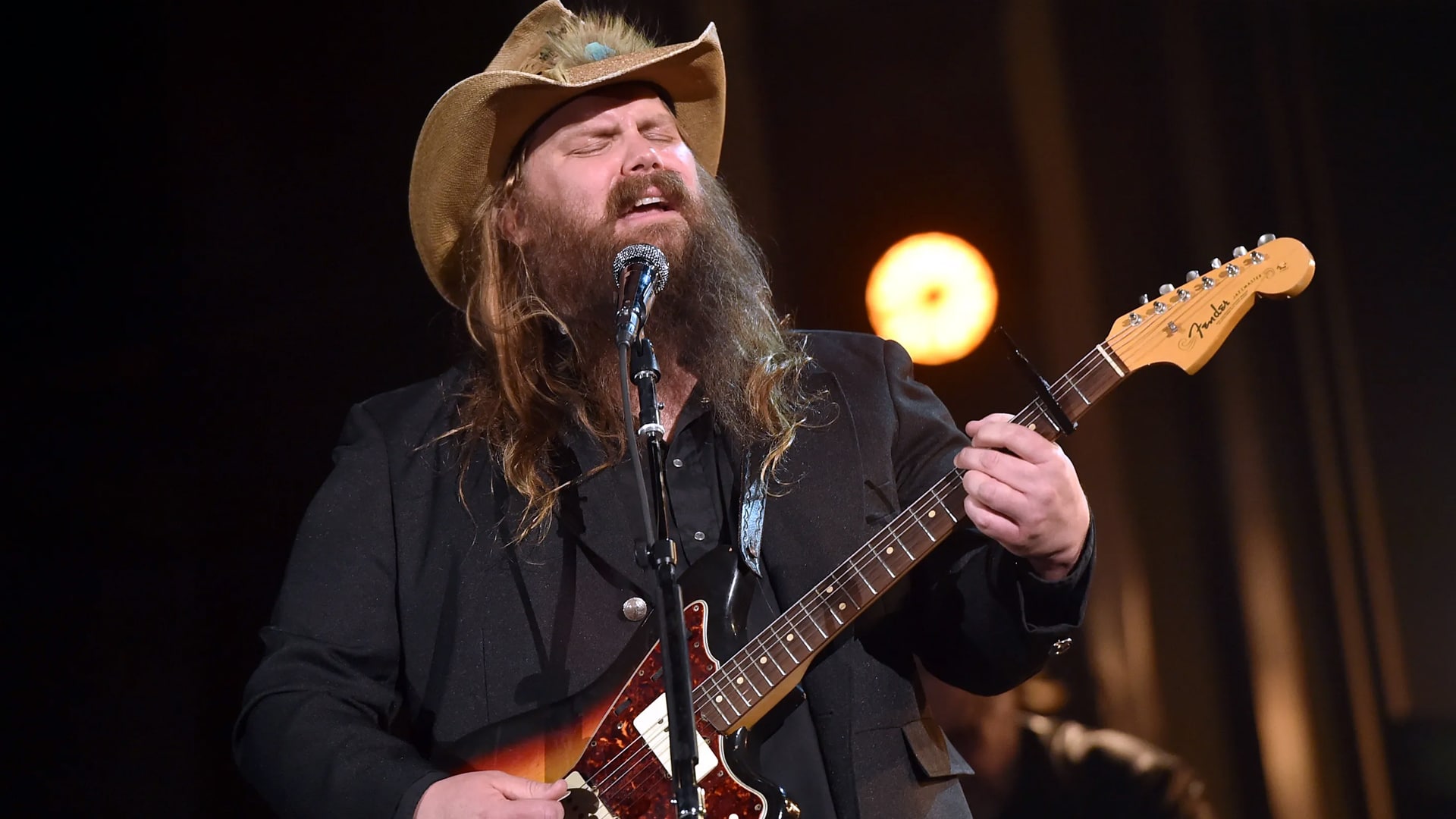 Chris Stapleton performing onstage in a cowboy hat and black suit while playing guitar, tied to his big $1 million donation to help Texas families after devastating floods.