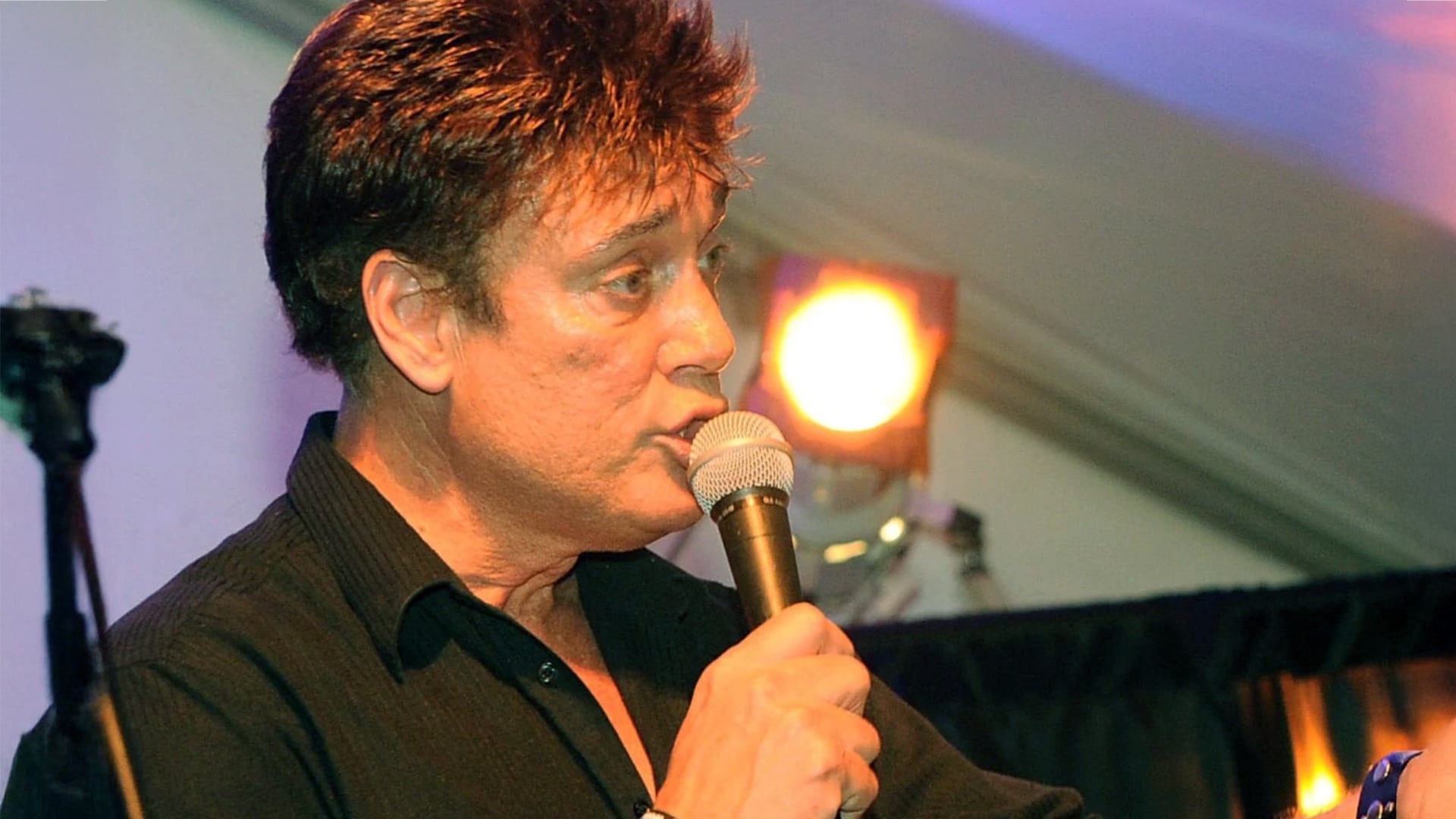 A few years ago, country singer Ronnie McDowell performs under stage lights, speaking into a microphone before his recent surgery complications.