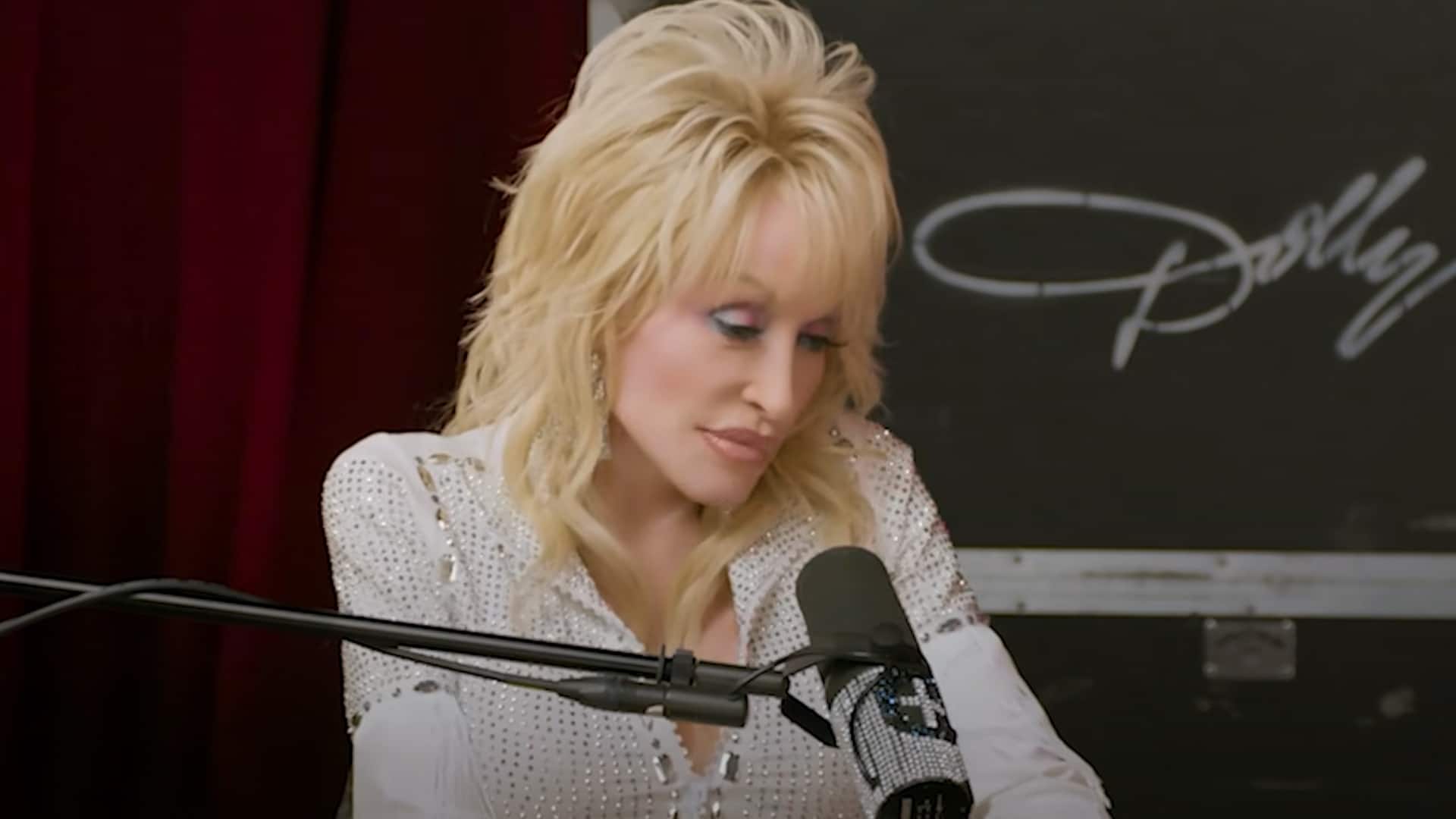 Dolly Parton looks down emotionally while speaking into a rhinestone-covered microphone during a candid moment on stage.