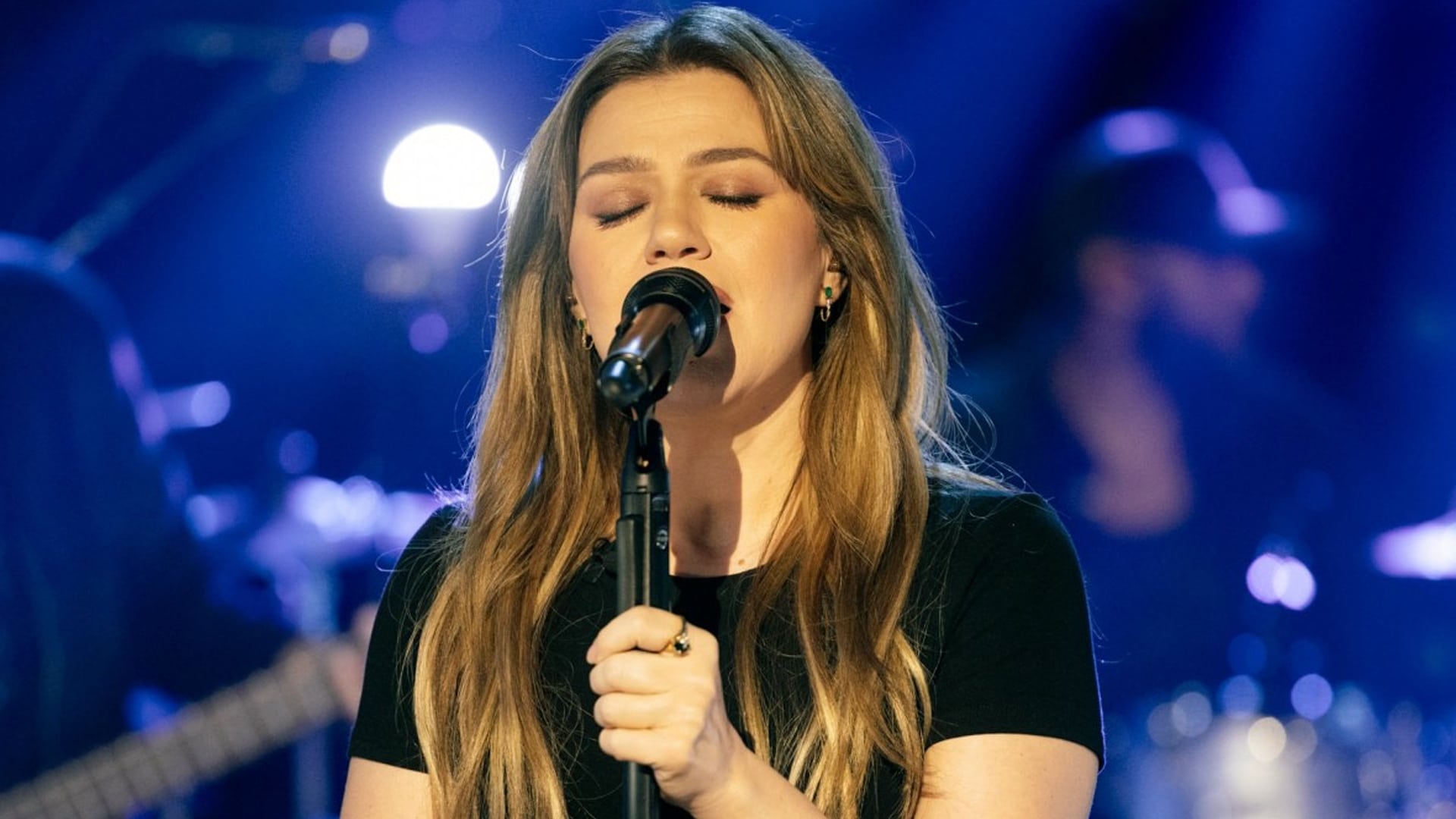 Kelly Clarkson closes her eyes while singing into a microphone during her raw performance of Cody Johnson’s “When It Comes To You.”