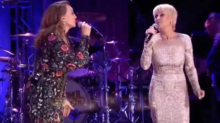 Pam Tillis and Lorrie Morgan share the stage in sparkling dresses, singing passionately into their microphones during a heartfelt duet.