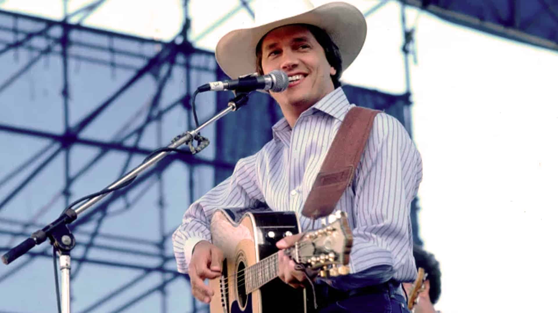 Young George Strait smiling on stage playing guitar in 1987 when “All My Ex’s Live in Texas” hit No. 1 and proved he ran country.