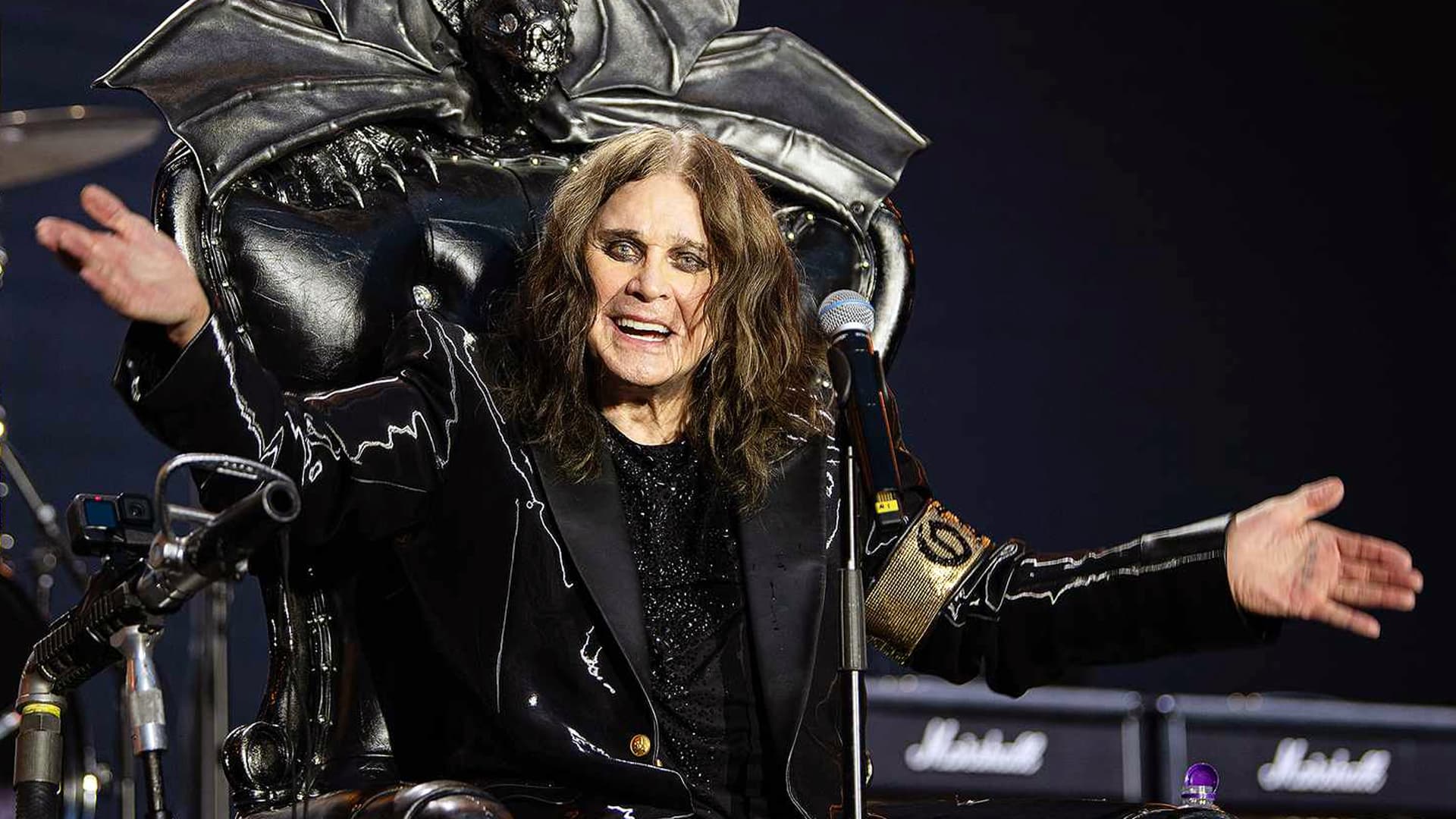 Ozzy Osbourne sits on a gothic throne with arms wide open, dressed in black with his signature smirk, capturing the legend's refusal to ever go country