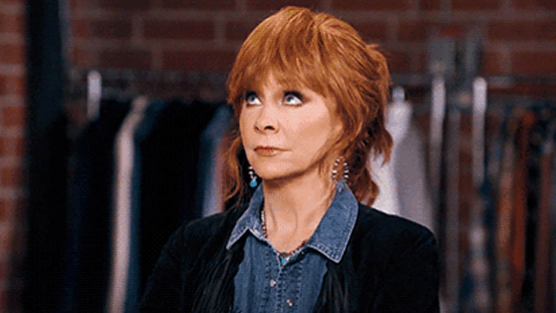 Reba McEntire rolls her eyes playfully while standing in front of a clothing rack, hinting at her off-camera personality.