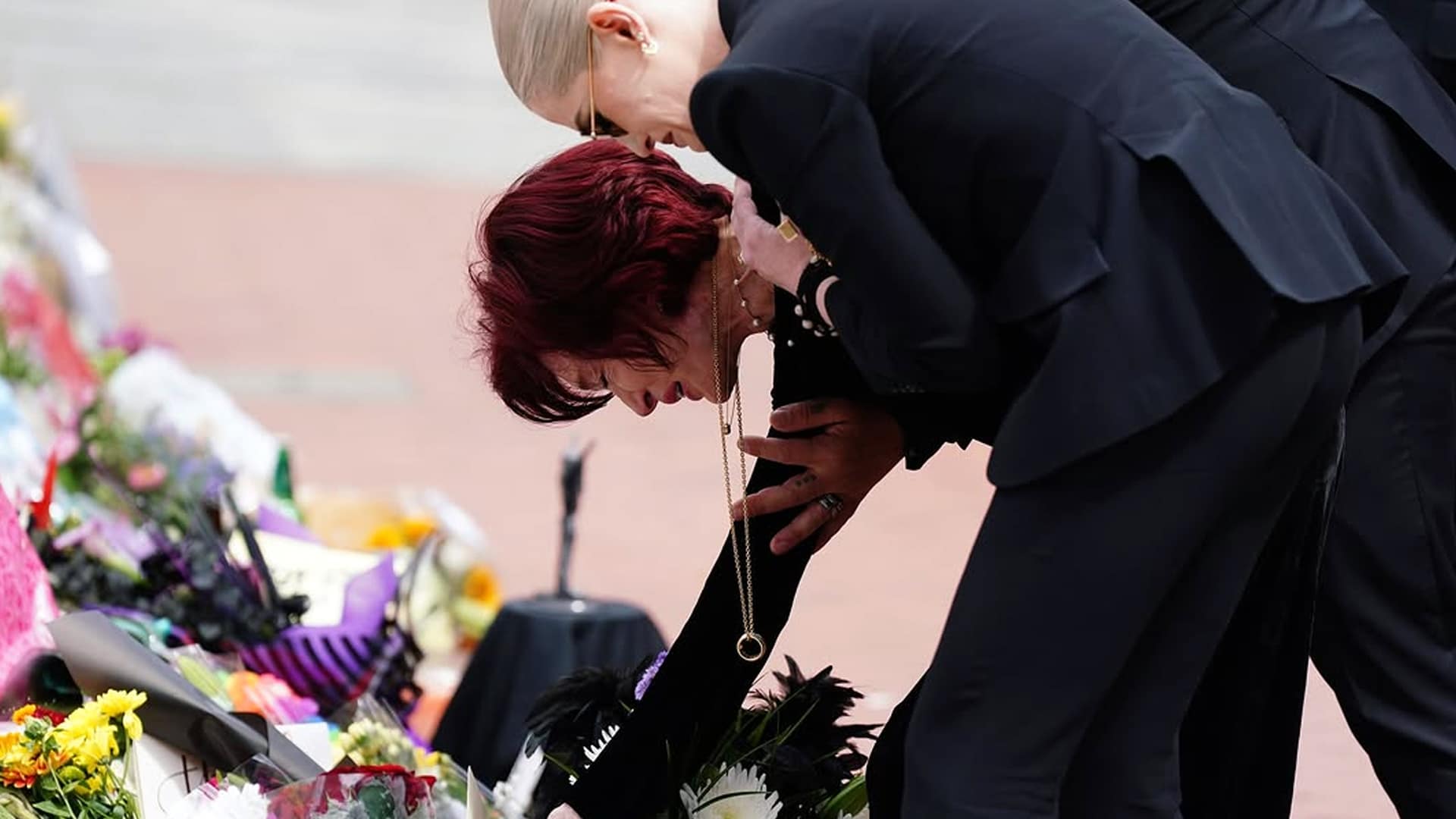Sharon Osbourne breaks down in tears while placing flowers during Ozzy Osbourne's funeral procession in Birmingham, surrounded by mourners.