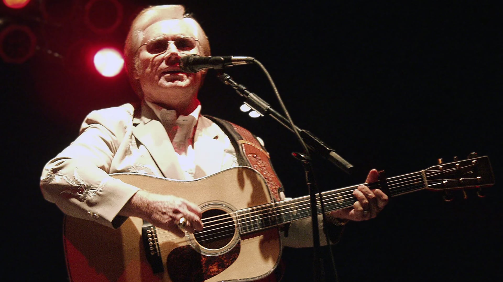 Country legend George Jones plays guitar under spotlight, embodying the raw heartbreak behind these 12 most depressing country songs.