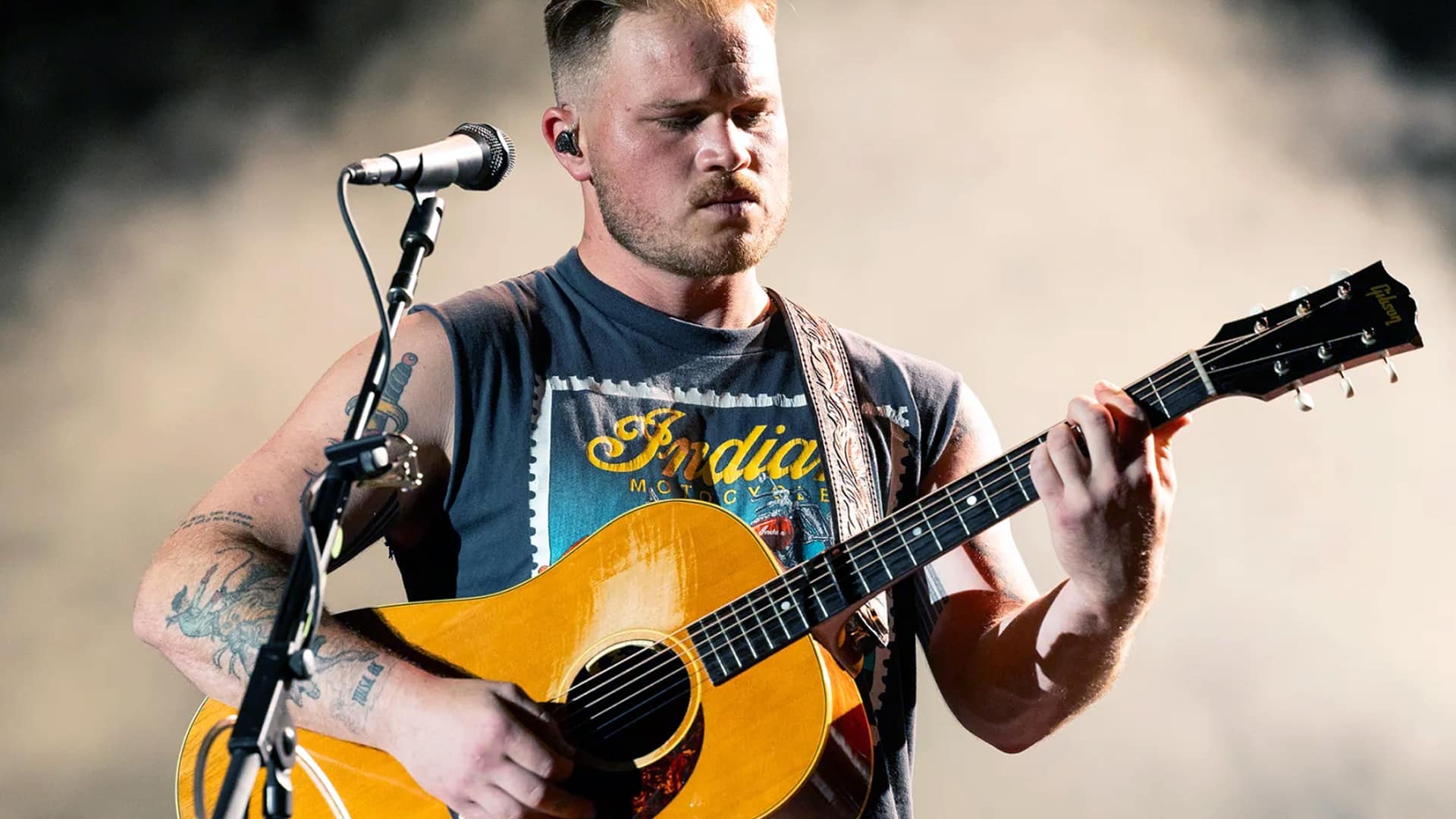 Zach Bryan plays guitar onstage in a past performance, as headlines today focus on his recent TikTok clash with a young fan.