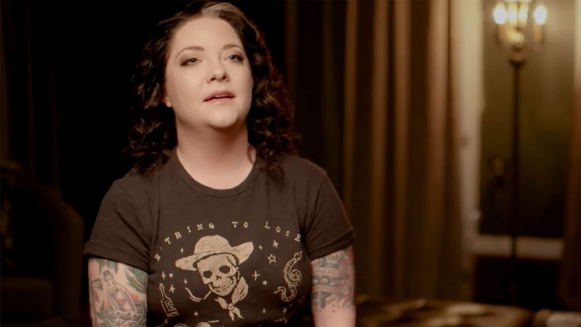Ashley McBryde, seen in a past interview setting, opens up about her recent vocal cord injury that will keep her silent for days while she works to keep her tour dates on track.