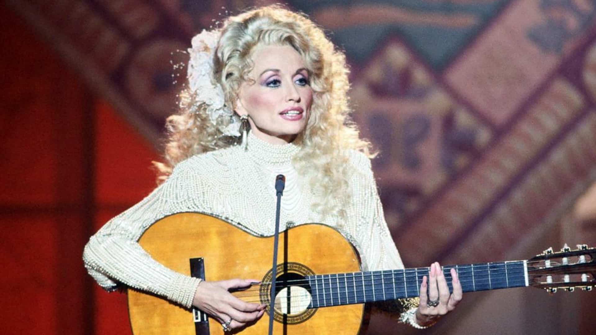 Dolly Parton performs “Coat of Many Colors” in a heartfelt throwback moment, wearing a pearl-studded top and strumming her guitar.