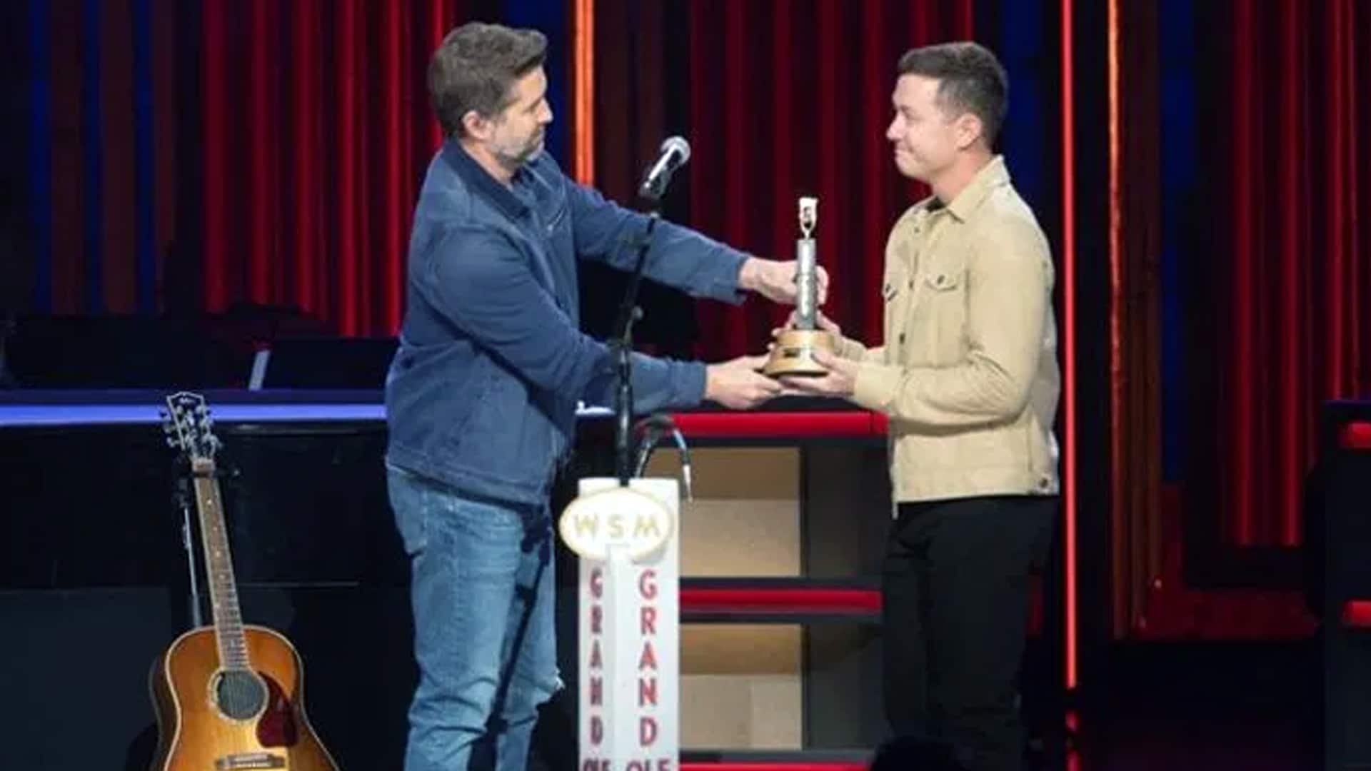 Scotty McCreery accepts his Opry award onstage as part of a tribute display honoring him, Josh Turner, and Randy Travis.