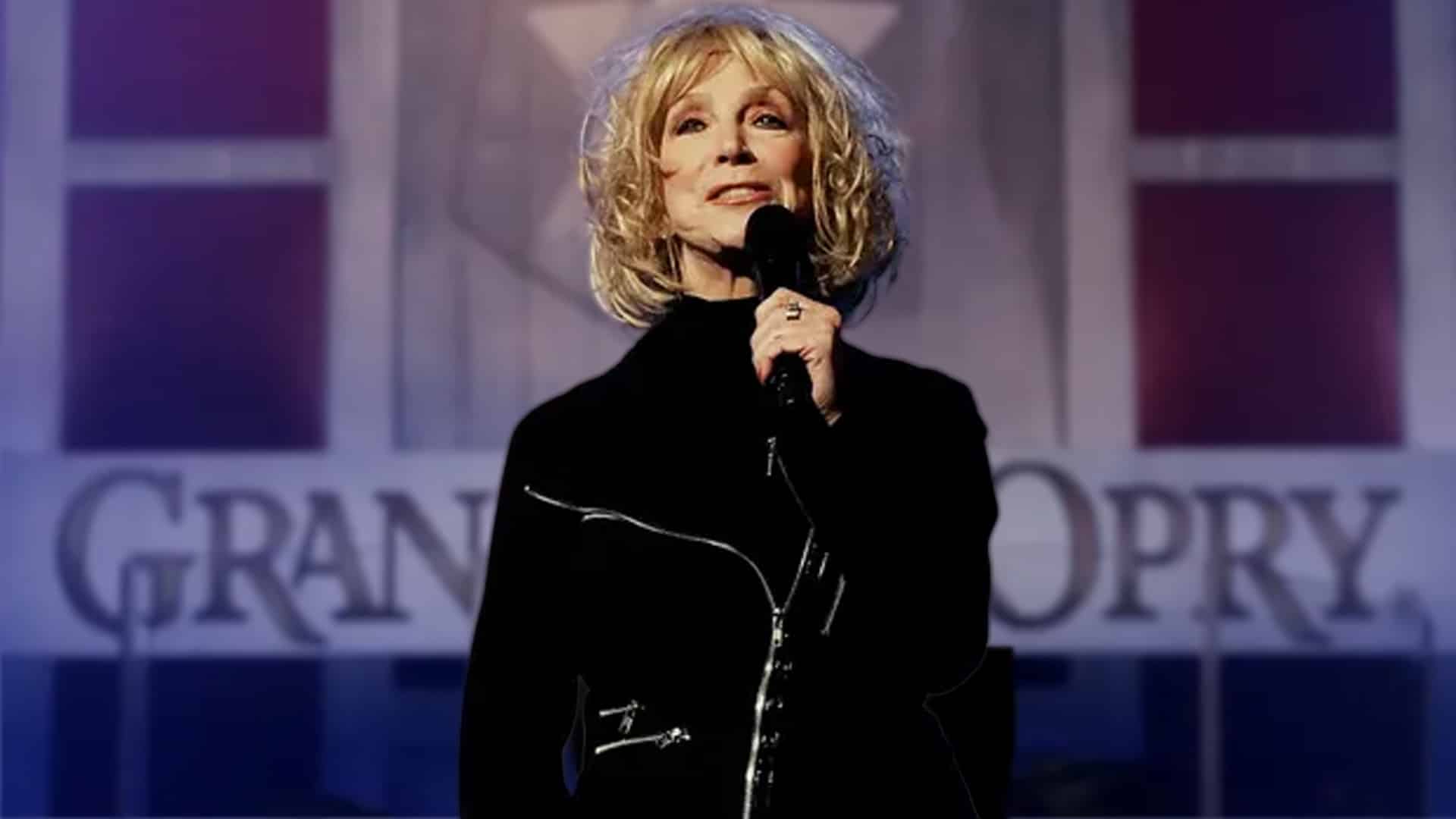 Jeannie Seely stands on the Grand Ole Opry stage holding a microphone, a fitting image for news on how fans can attend or stream her upcoming celebration of life.