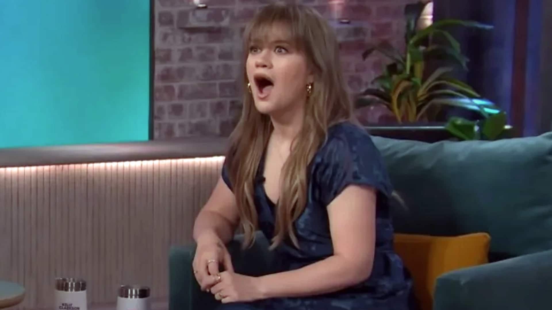 Kelly Clarkson sits on her talk show couch with a shocked expression after learning that Garth Brooks used to be a bouncer before his country music fame.