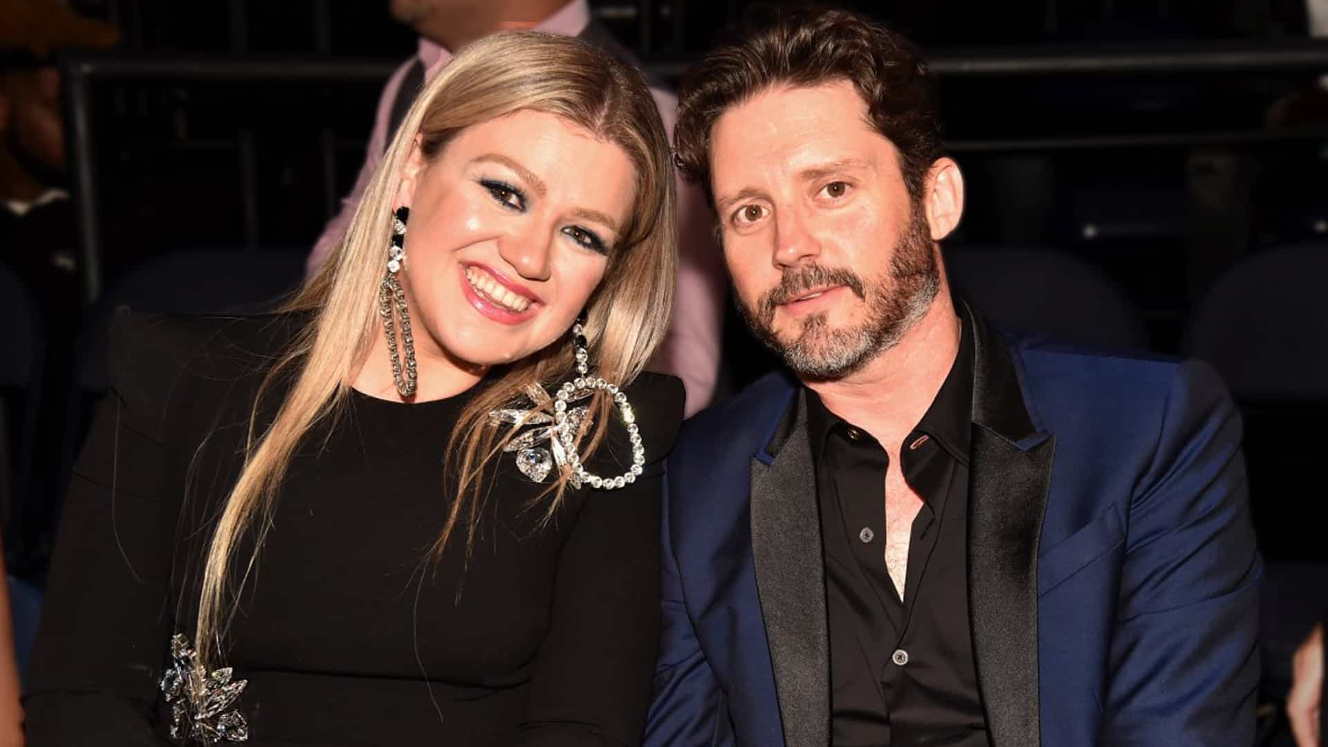 Kelly Clarkson smiling beside Brandon Blackstock at a public event, years before their divorce that insiders say was far more complicated than “irreconcilable differences.”