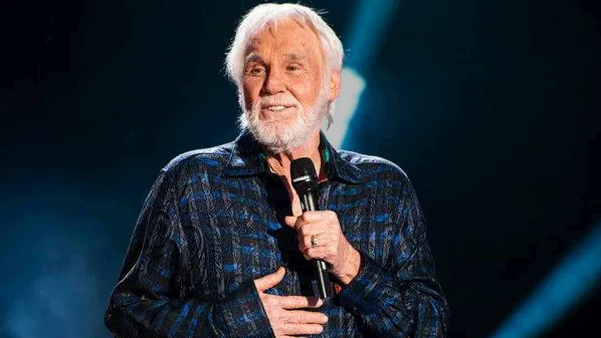 Kenny Rogers smiling onstage with a microphone in hand, a reminder of the country icon’s journey from poverty to legend.